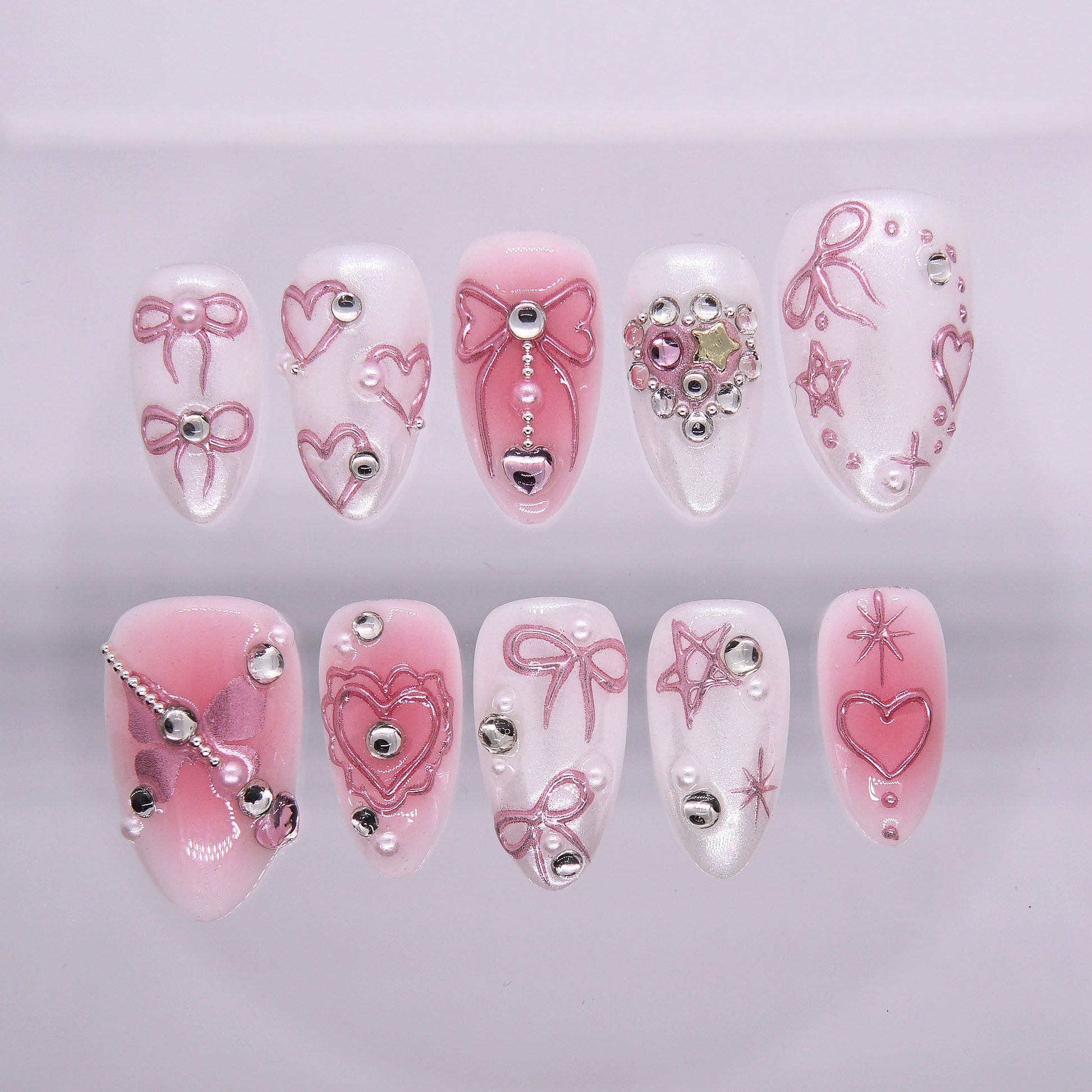 Girly pink and white chrome press-on nails with 3D bows, hearts, stars, and rhinestone details from Nailsium’s Wood · Bloom collection.
