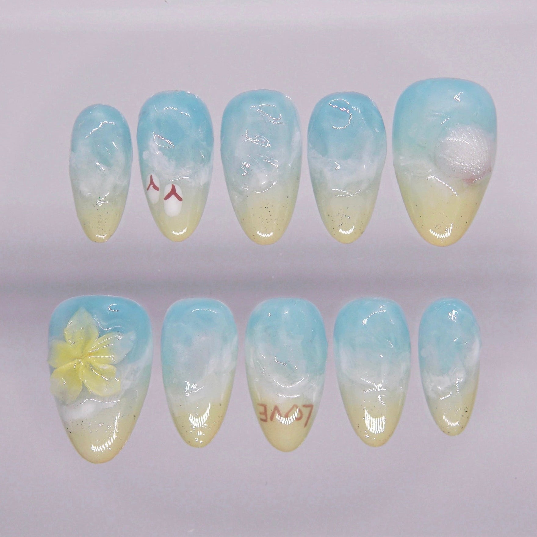 Press on nail set inspired by ocean waves and sandy beaches, featuring blue foam designs with yellow tips and summer charms.