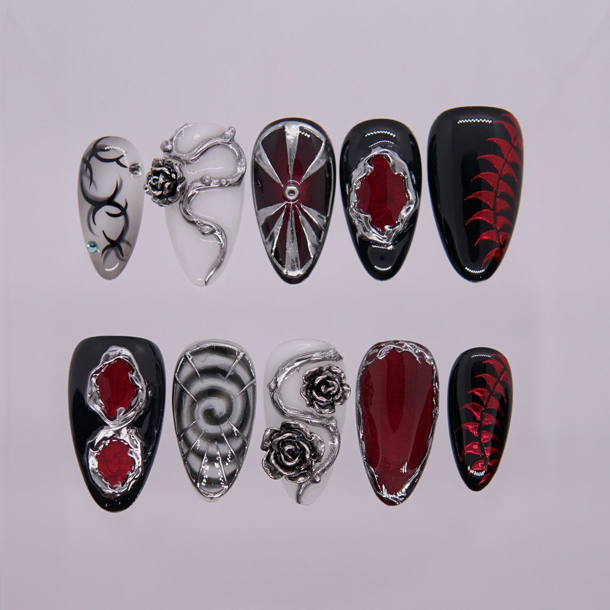 Cinnabar Relic press-on nails — black, white, and red with chrome roses and molten silver frames.