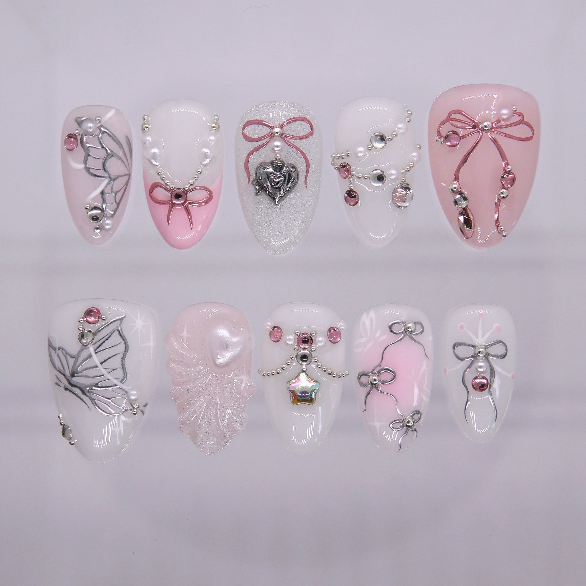 Pink and white press on nails decorated with ribbons, pearls, and heart charms in a dreamy fairytale style.