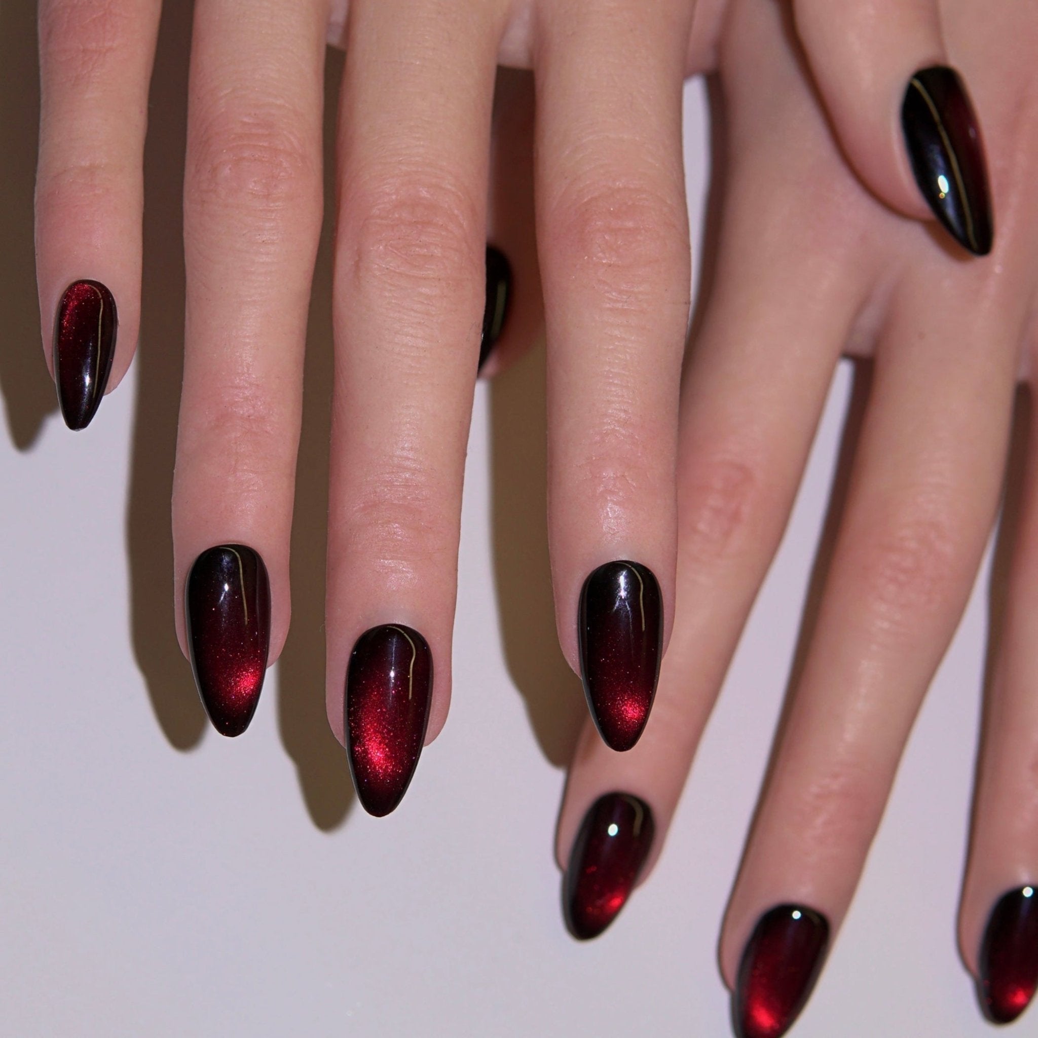 Close-up of molten red and black cat-eye press-on nails glowing under light, inspired by fiery transformation and Halloween energy.