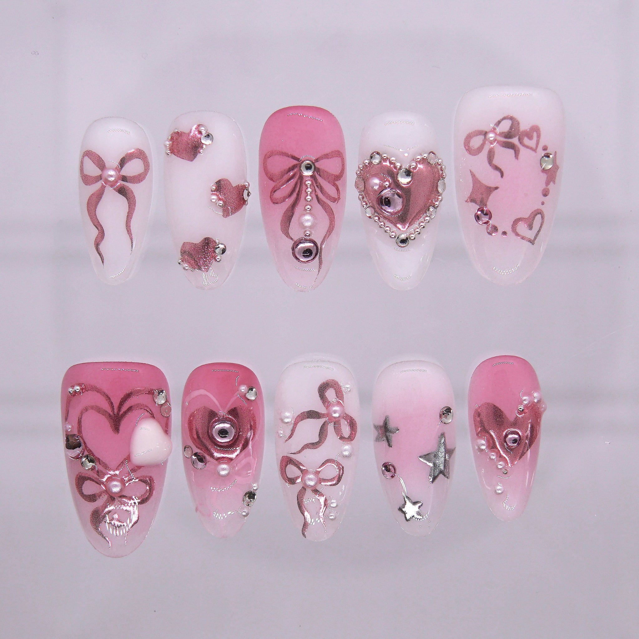 Pink press on nails decorated with metallic bows, hearts, pearls, and stars for a playful party look.