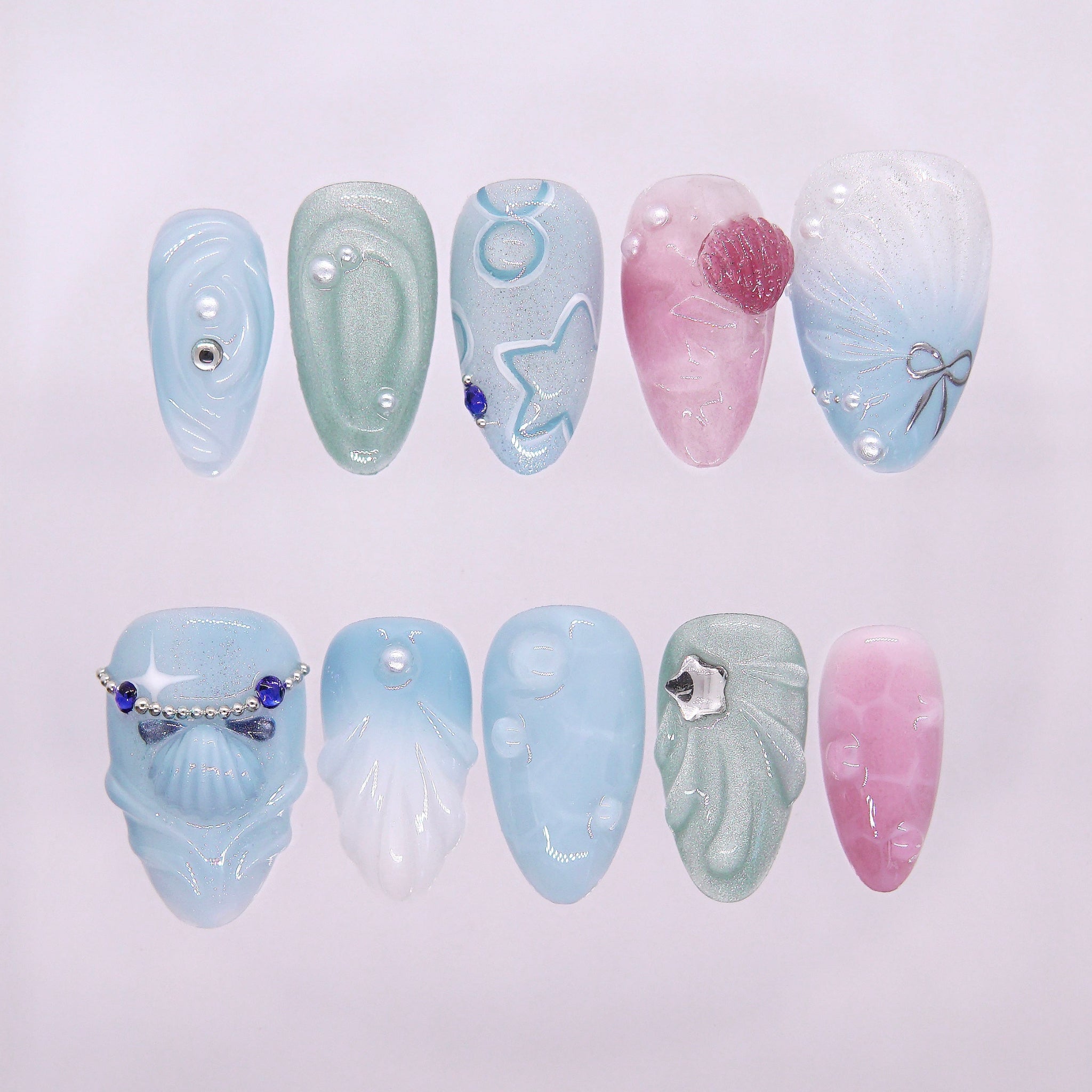 Tidepool Walk press-on nails with soft seafoam-to-pink gradient, featuring iridescent shell pieces, silver star glitters, and water droplet accents — part of the La Jolla · Water · Flow collection.