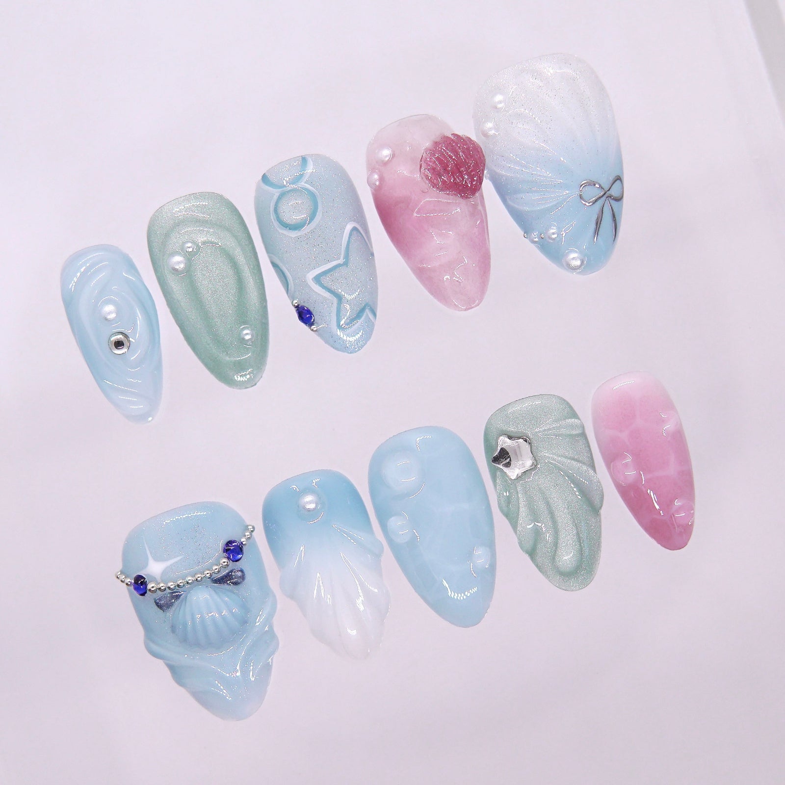 Tidepool Walk press-on nails with soft seafoam-to-pink gradient, featuring iridescent shell pieces, silver star glitters, and water droplet accents — part of the La Jolla · Water · Flow collection.