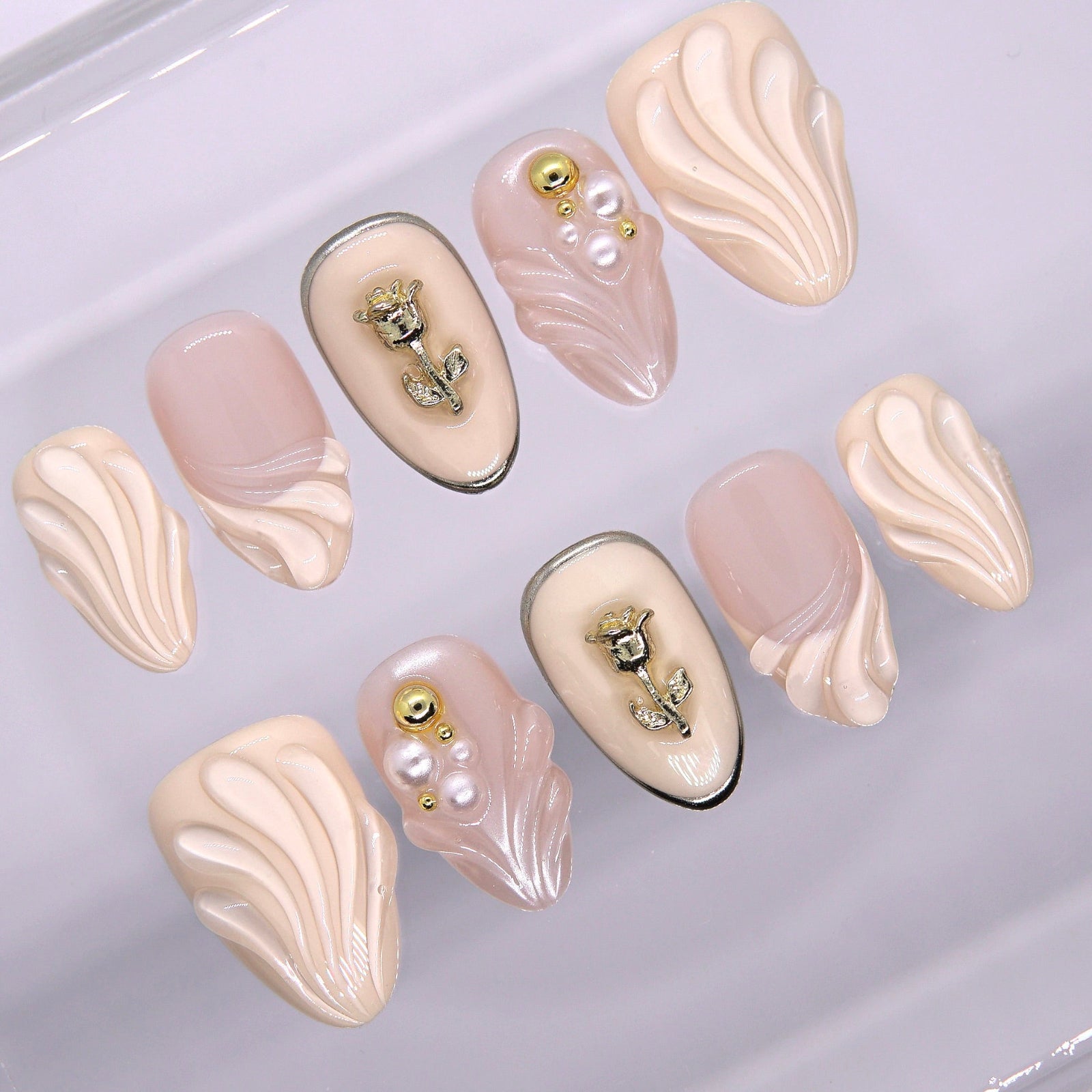 Close-up of pearl and rose gold charm on soft nude press-on nail with carved floral texture.