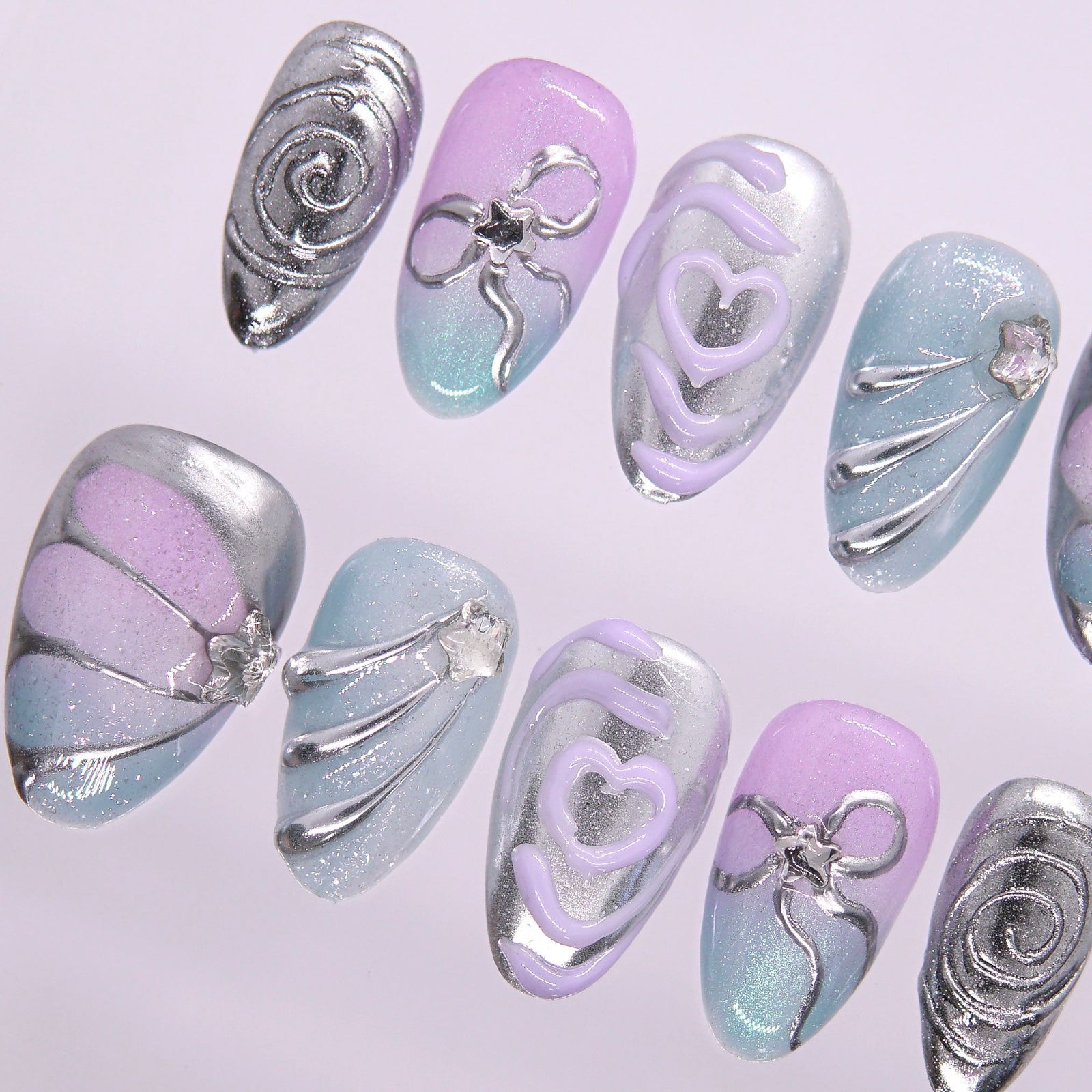 Flat lay of a pastel chrome nail set featuring sculptural silver lines and gradient tones.