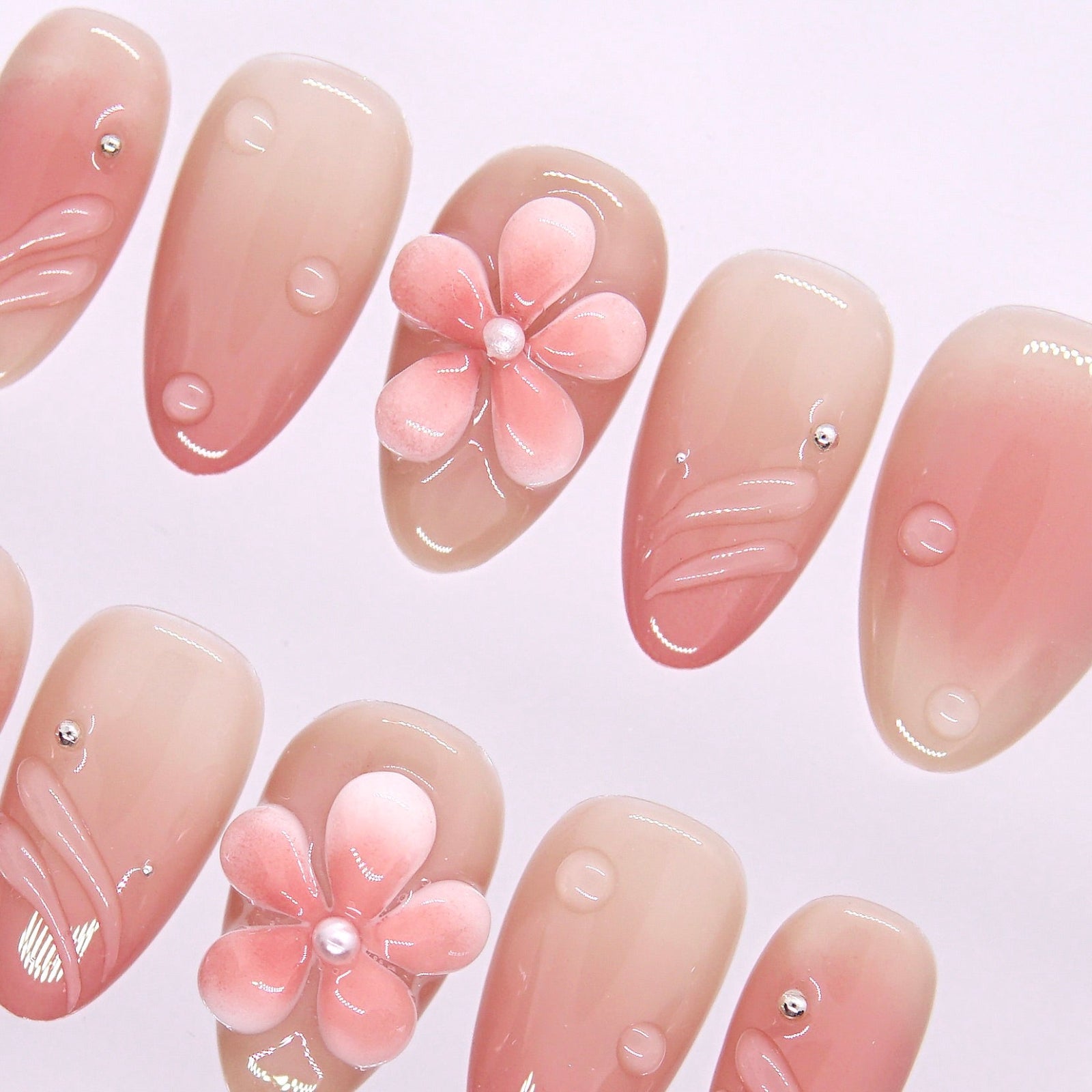 Close-up of pearl-centered flower and clear dew-drop texture on nude-pink gradient press-on nails.