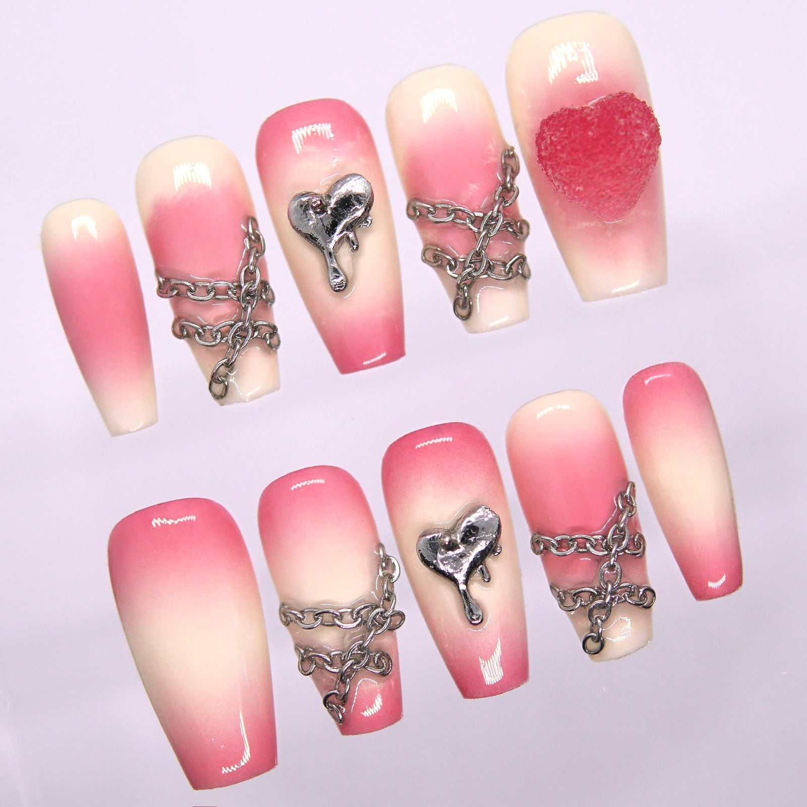 Close-up of silver chains and dripping heart charm on pink gradient press-on nails.