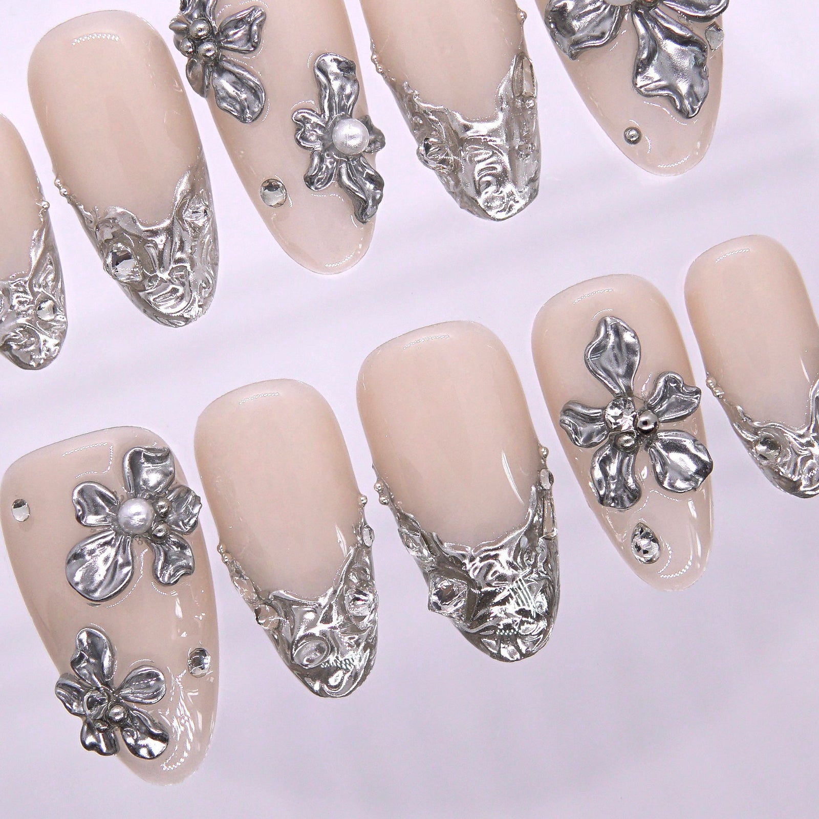 Macro view of silver cuticle detailing on a nude nail, highlighting architectural floral scrolls inspired by wedding lace and coastal stonework.
