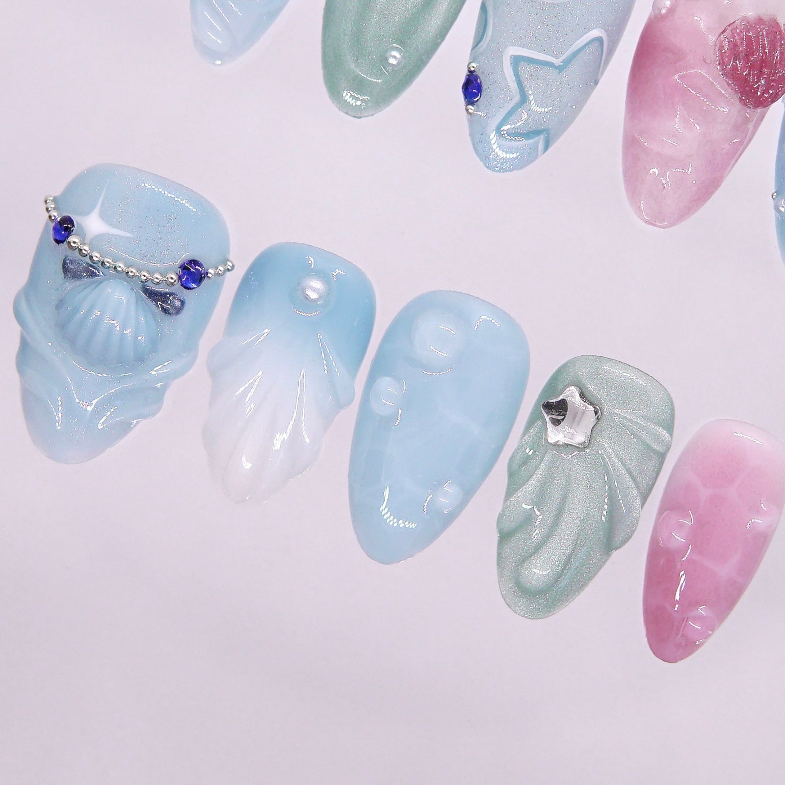 Close-up of translucent nail with seashell shard and silver microchain, capturing a tidal treasure vibe.