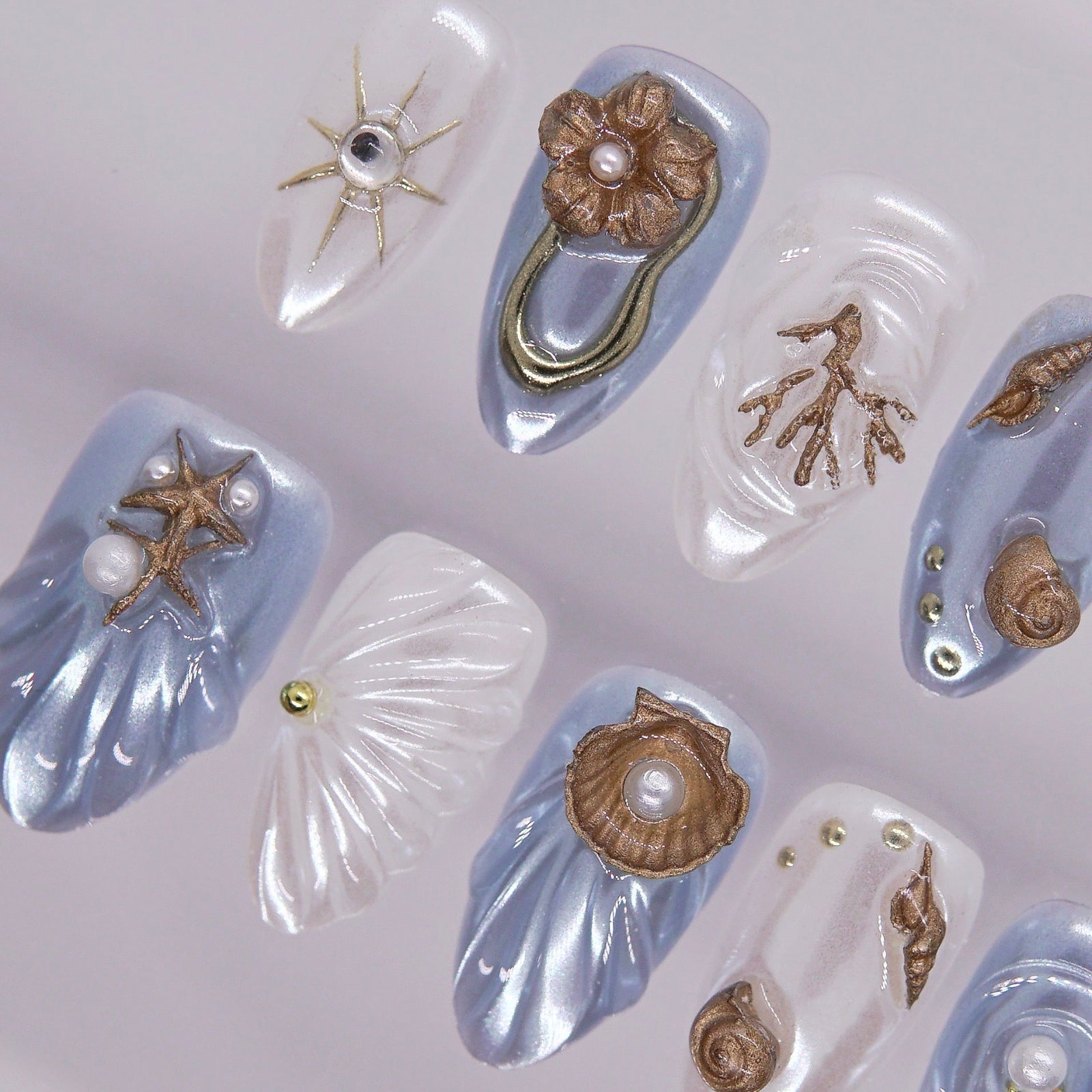 Blue and white sculpted nails with coral branches, shell ridges, and metallic gold details.