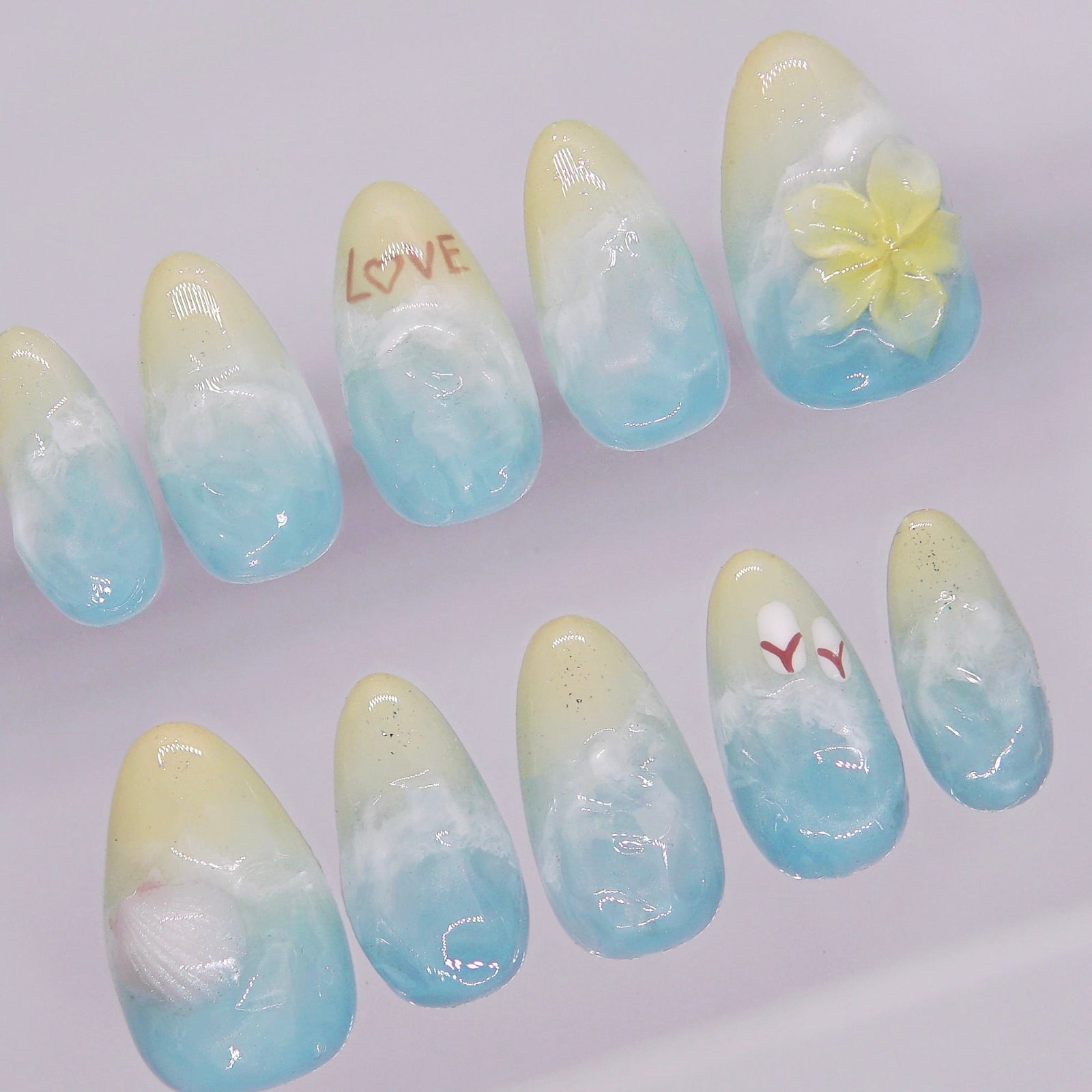 Close-up of nail design with “LOVE” written in the sand effect on beach-inspired press on nails.