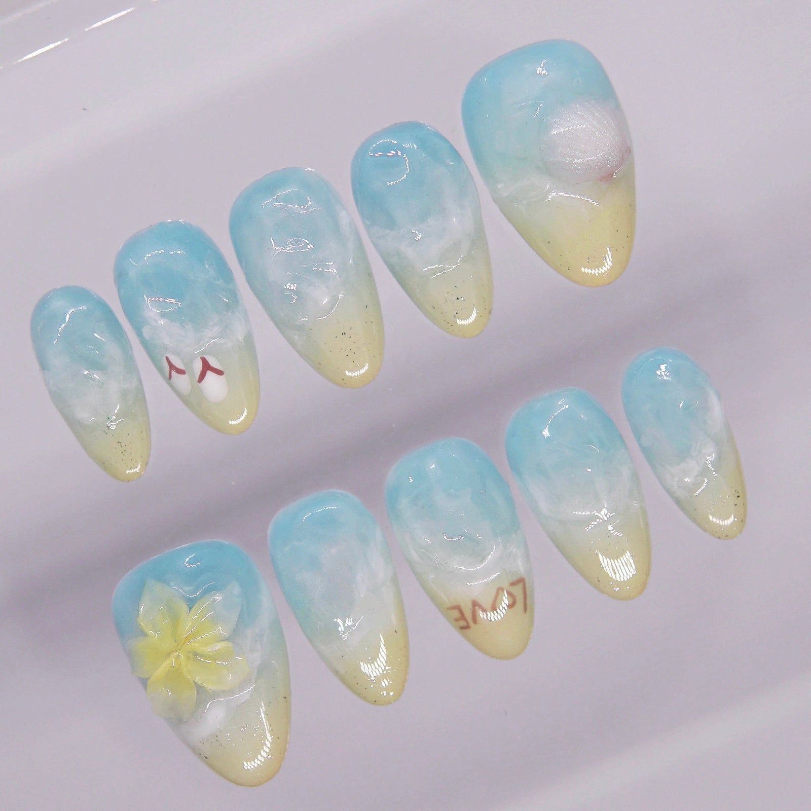 Seashell and flower embellishments on beach wave press on nails with ocean gradient.