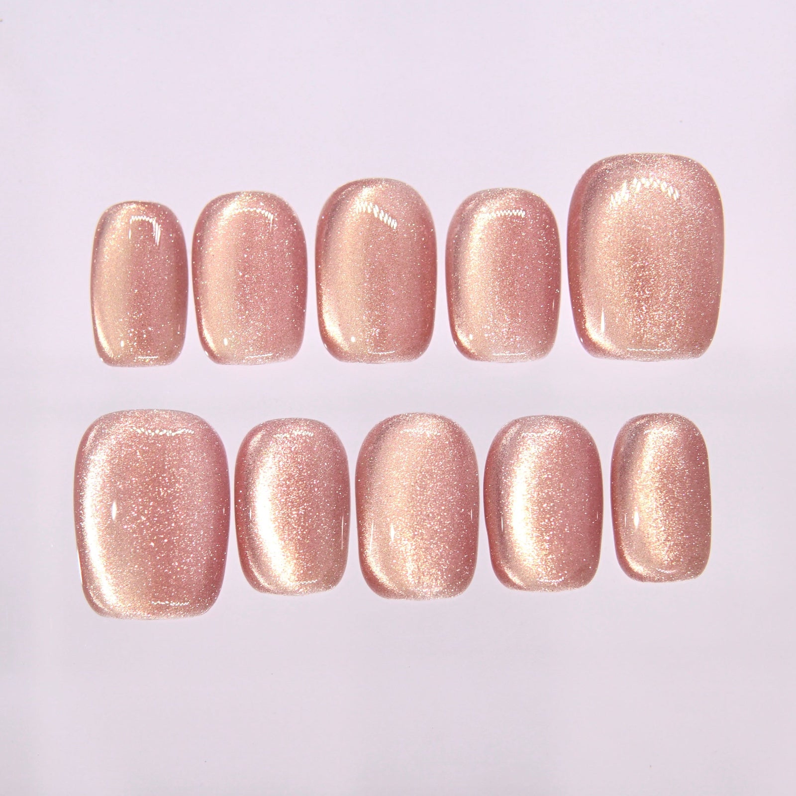 Soft peach pink cat eye press on nails arranged on clear display board with luminous shimmer