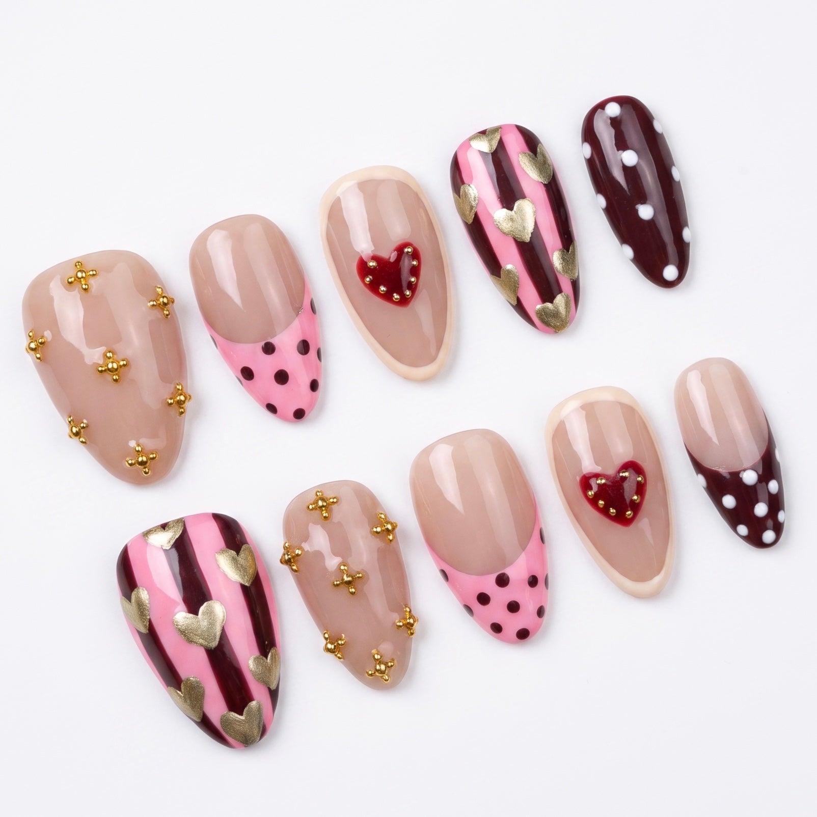 Close-up of Liberty Horse press-on nails featuring striped pink and burgundy patterns with gold heart accents.
