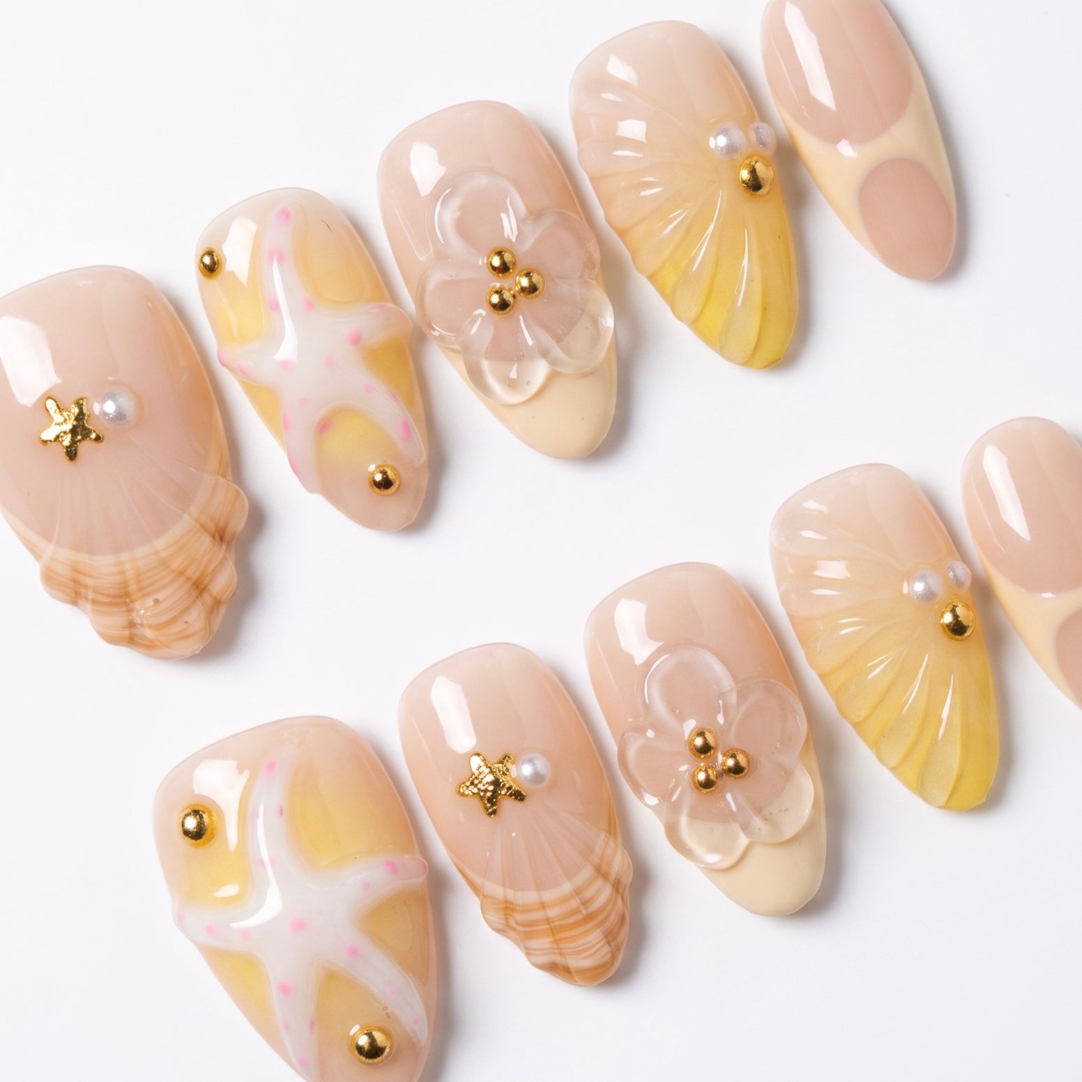 Close-up of handmade seashell press-on nails featuring sculpted shell textures, tiny flowers, pearls, and gold embellishments.
