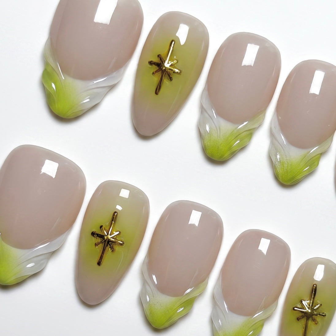 Close-up of handmade nude and lime French tip nails with gold star embellishments and glossy finish.
