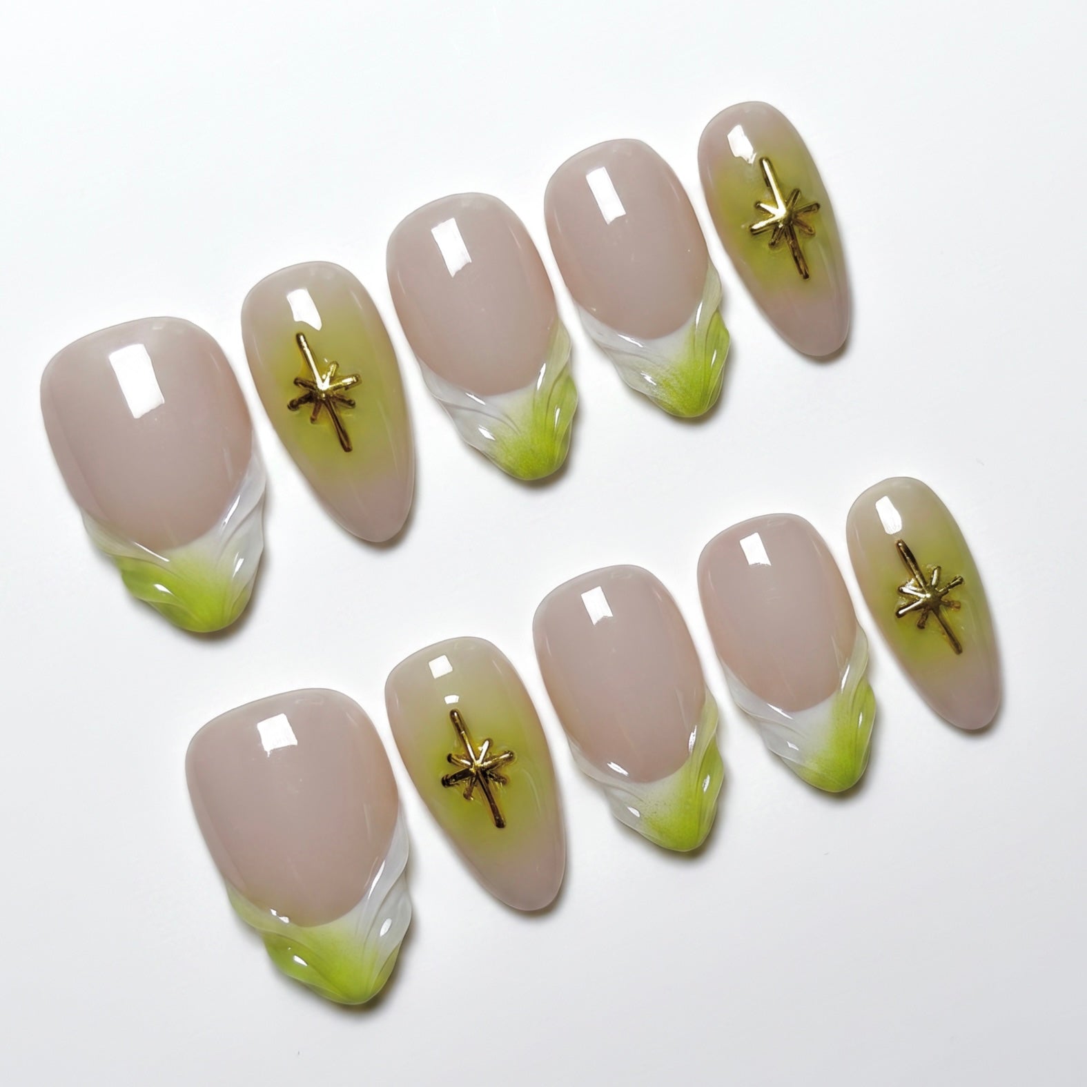 Close-up of handmade nude and lime French tip nails with gold star embellishments and glossy finish.
