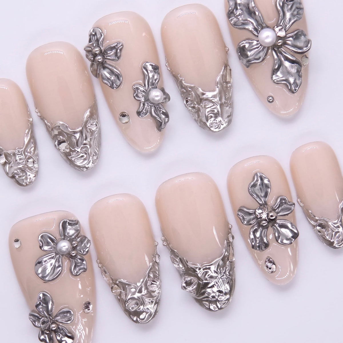Macro view of silver cuticle detailing on a nude nail, highlighting architectural floral scrolls inspired by wedding lace and coastal stonework.