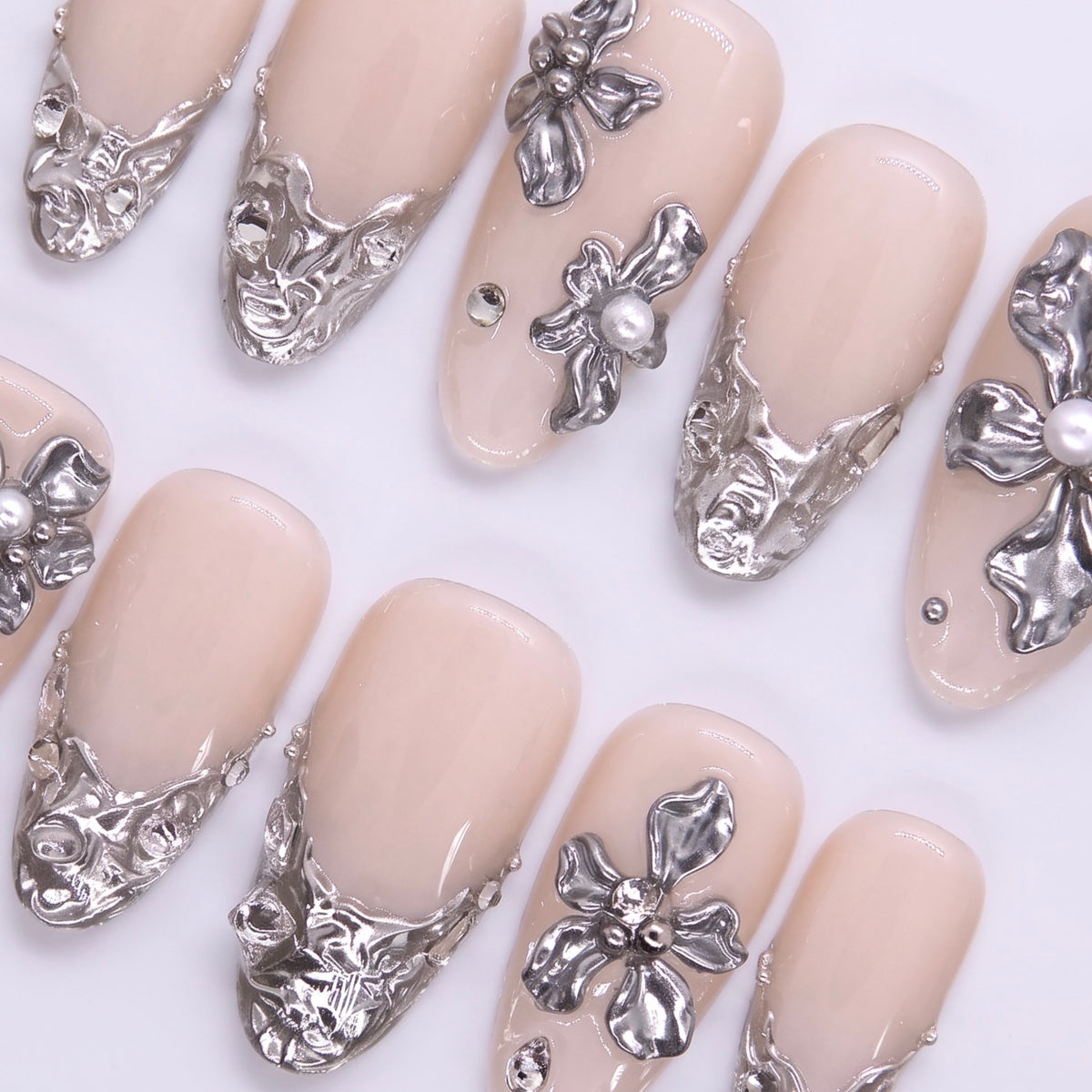 Close-up of large metallic silver floral embellishment on nude nail surface, showcasing detailed carving and pearl-like structure.