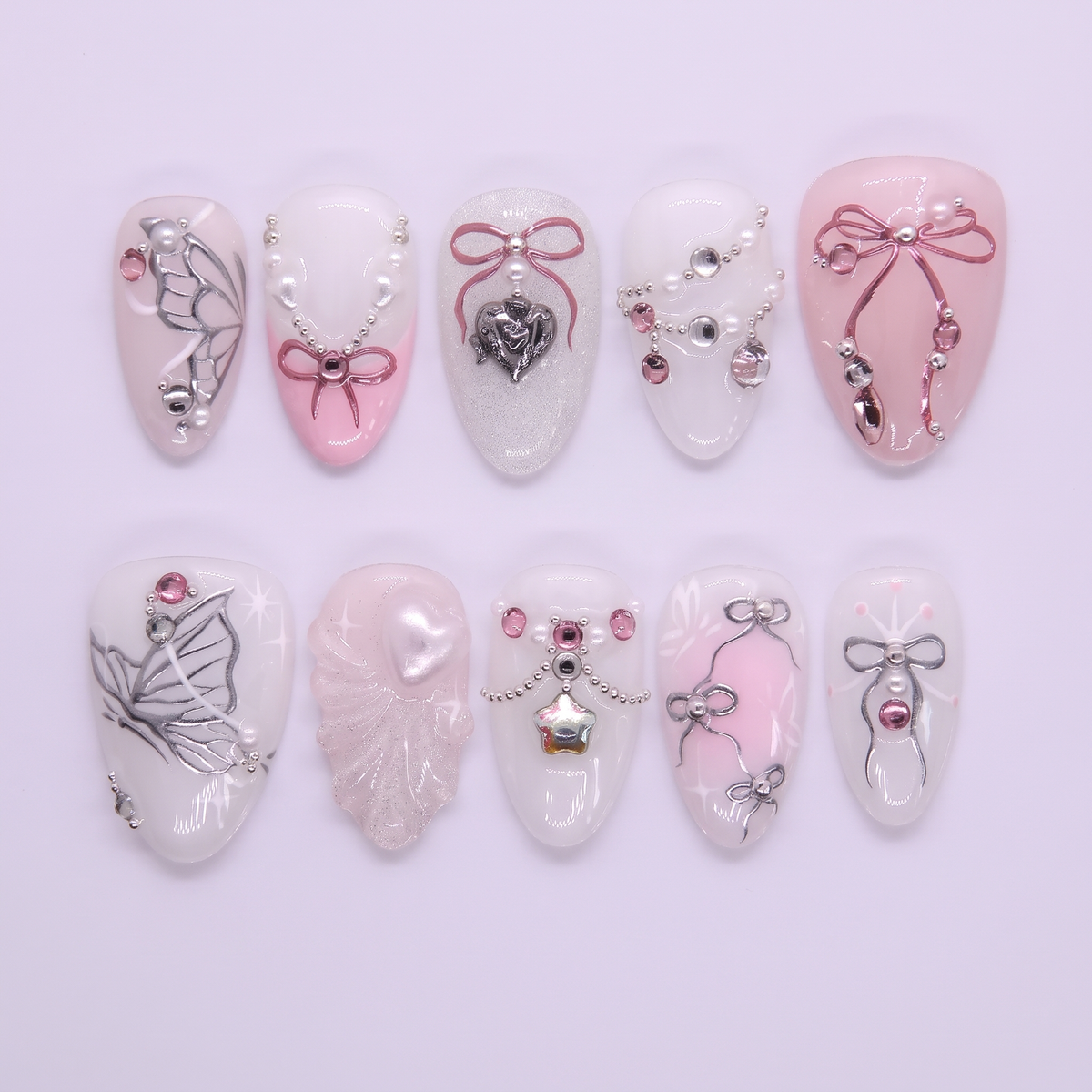 Pink and white press on nails decorated with ribbons, pearls, and heart charms in a dreamy fairytale style.