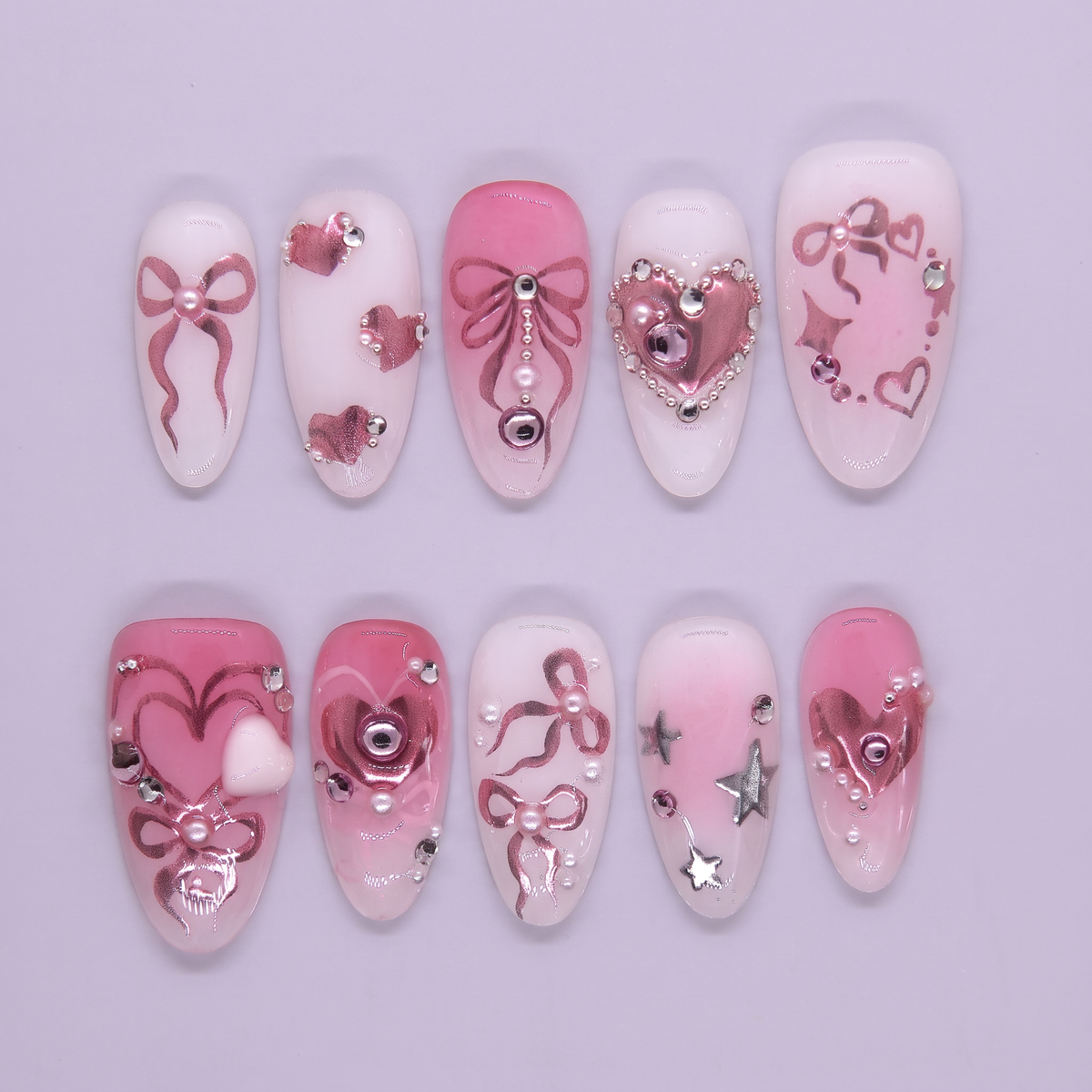 Pink press on nails decorated with metallic bows, hearts, pearls, and stars for a playful party look.