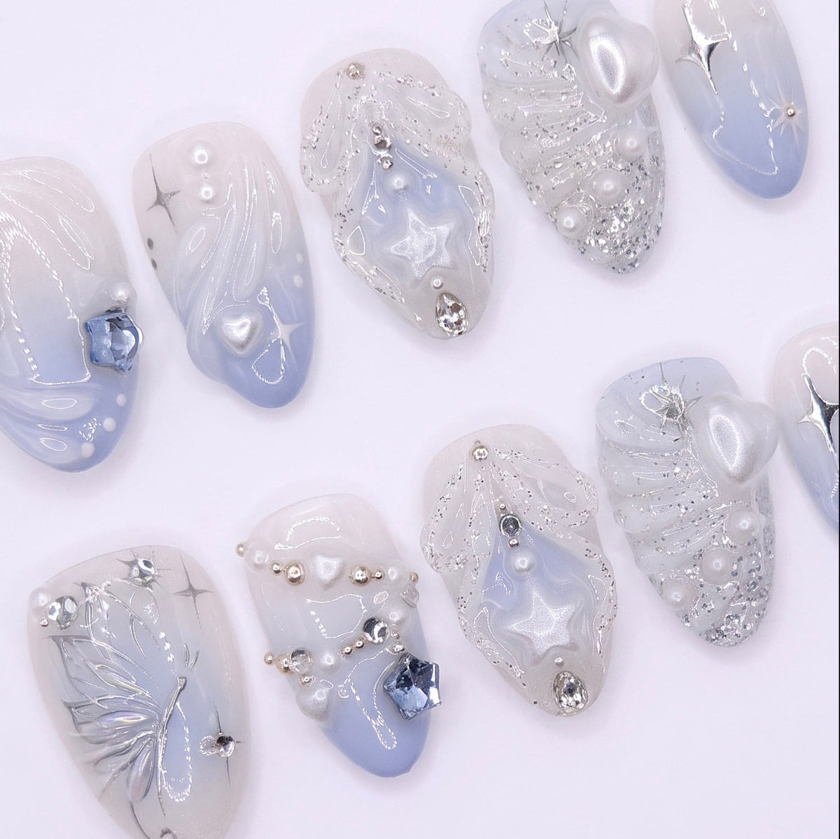 Soft pearly white and icy blue press-on nails with glowing pearls and glitter accents.