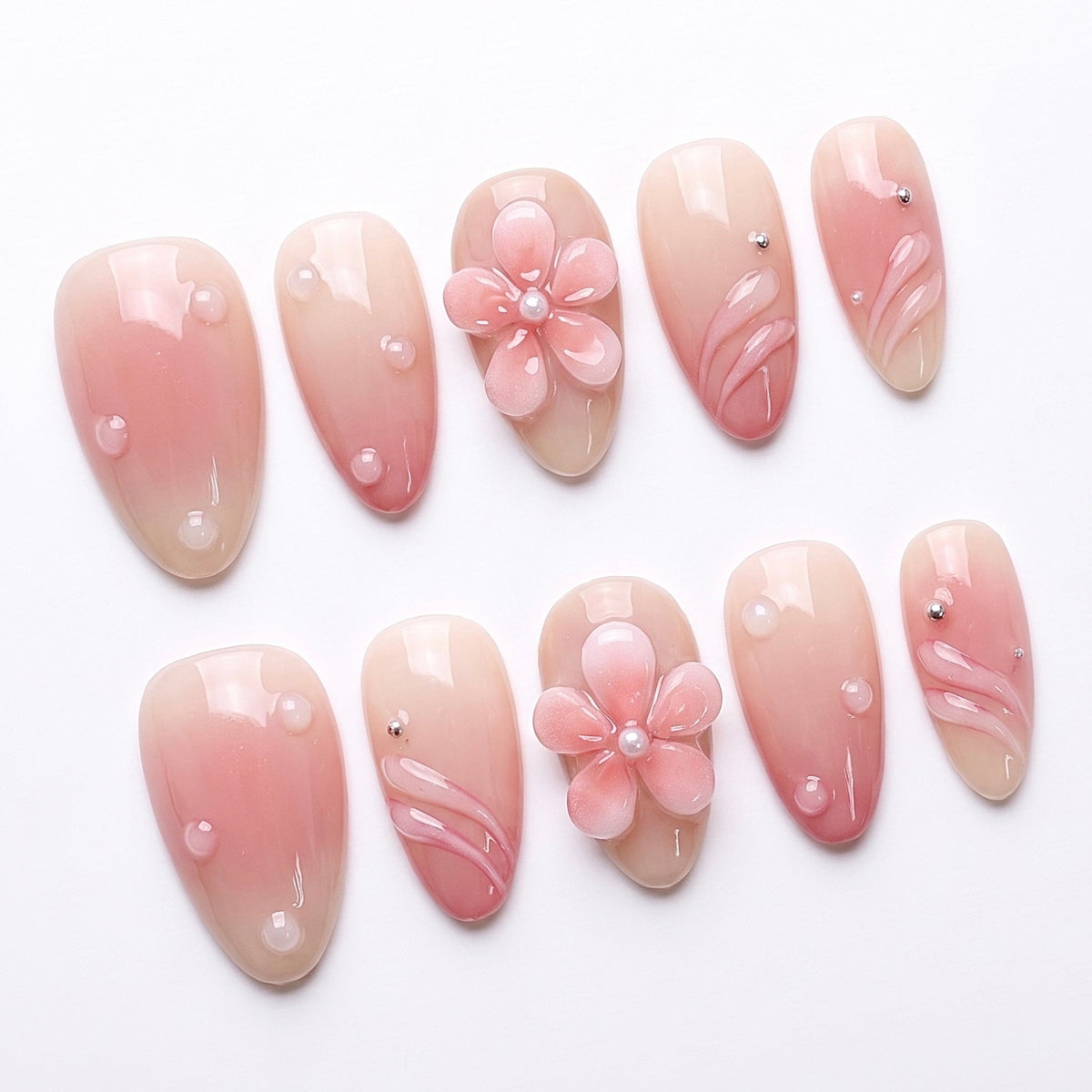 Close-up of pearl-centered flower and clear dew-drop texture on nude-pink gradient press-on nails.