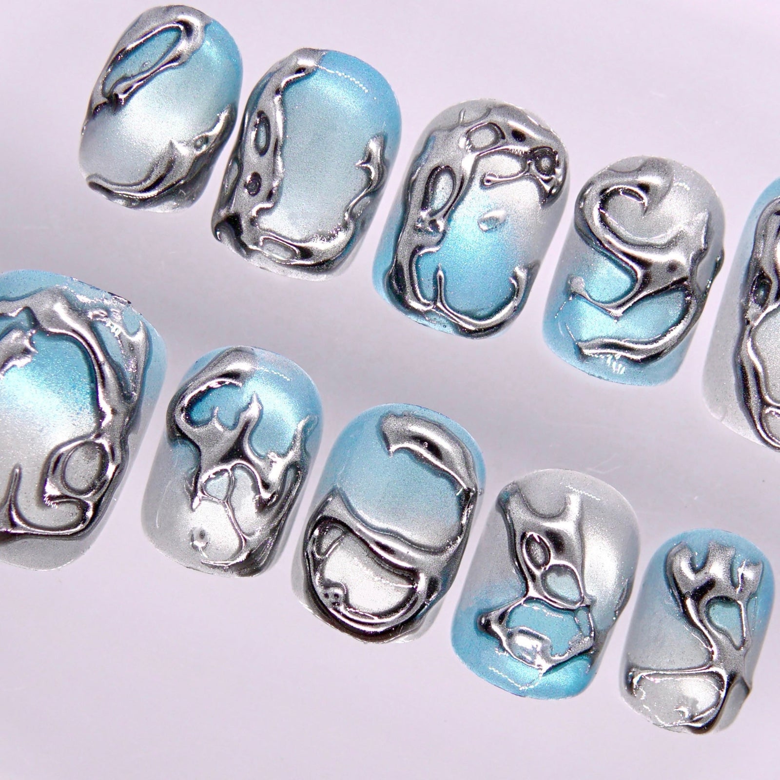 Detail view of Begin in Motion press-on nails highlighting organic, water-inspired metallic curves and modern texture