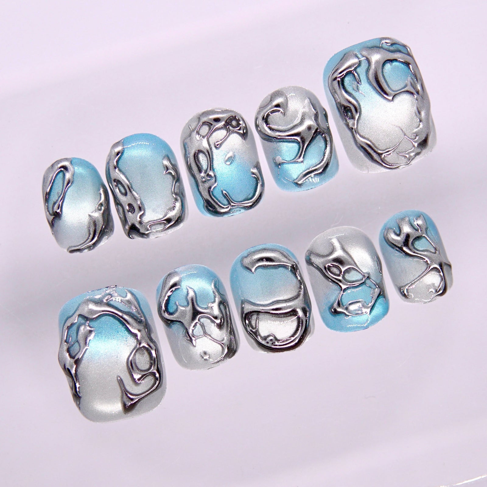 Close-up of Begin in Motion press-on nails showing sculptural silver lines flowing across cool blue gradient base