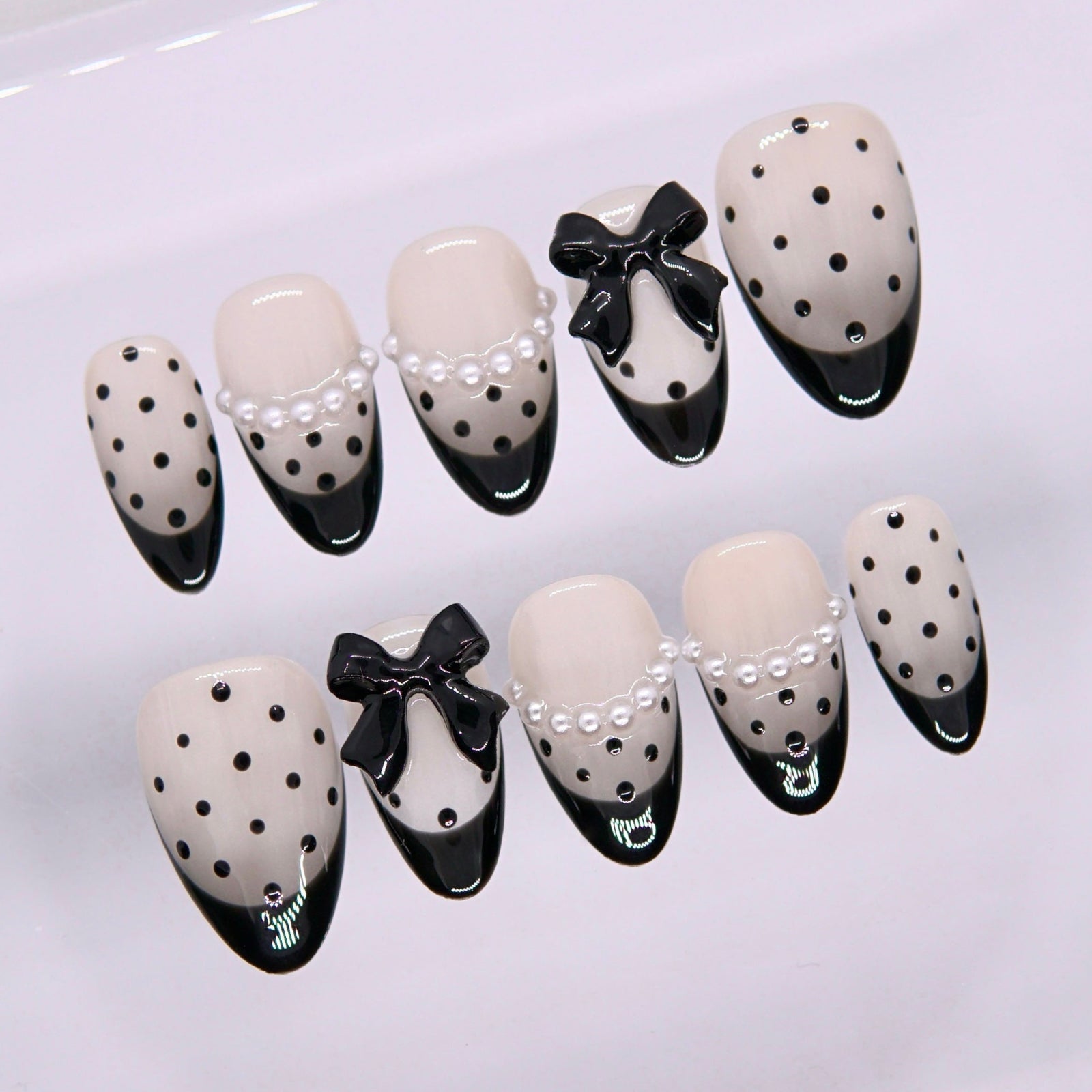 Close-up of Begin with Intention press-on nails showing pearl embellishments, black bow accents, and classic polka dot pattern