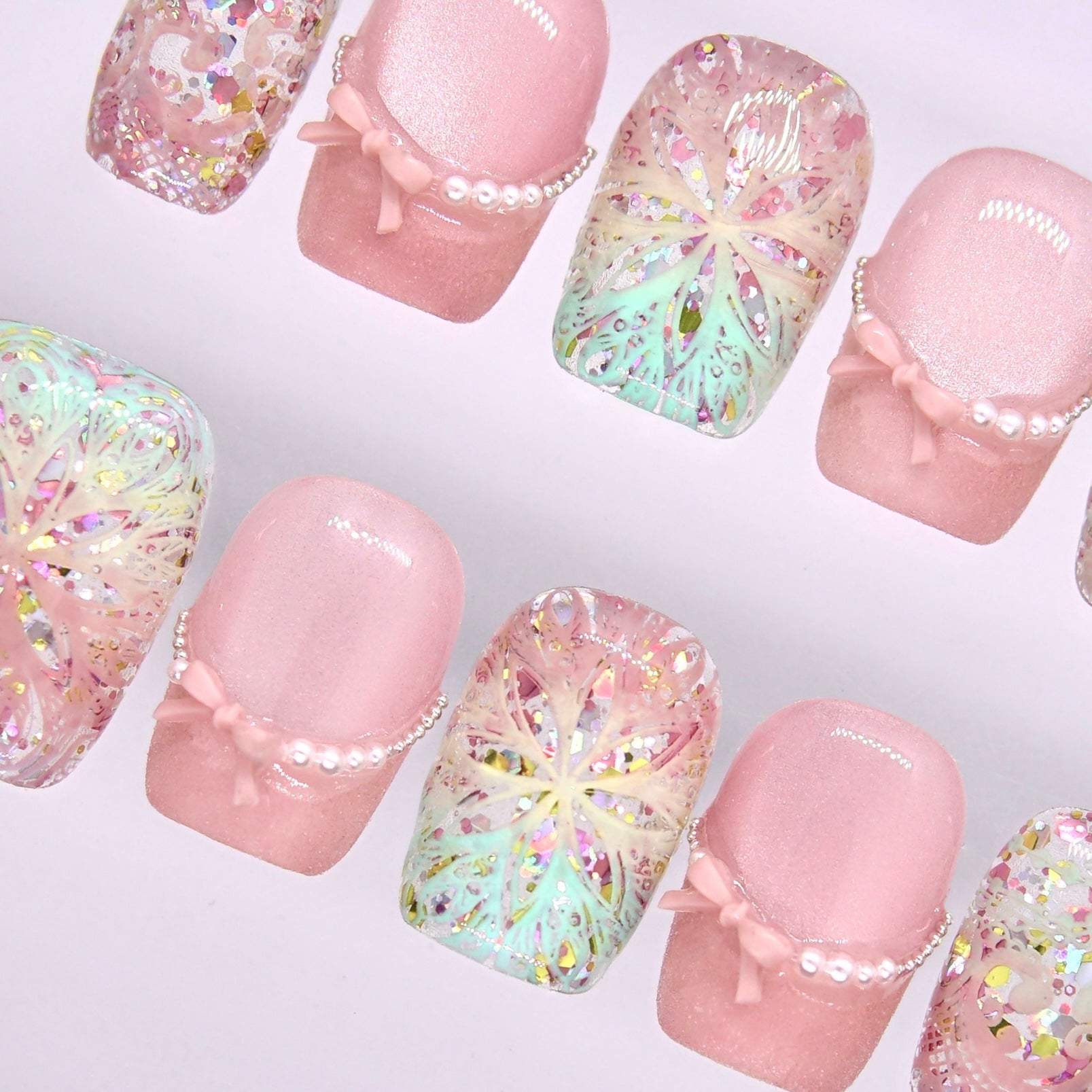 Detail view of Begin Infinite press-on nails featuring soft pink nails with delicate bow accent and light-reflecting glitter finish