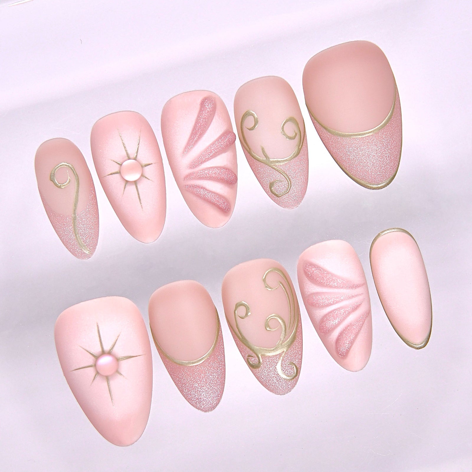 Close-up of Begin with Trust press-on nails showing gold celestial symbols and delicate blush pink base