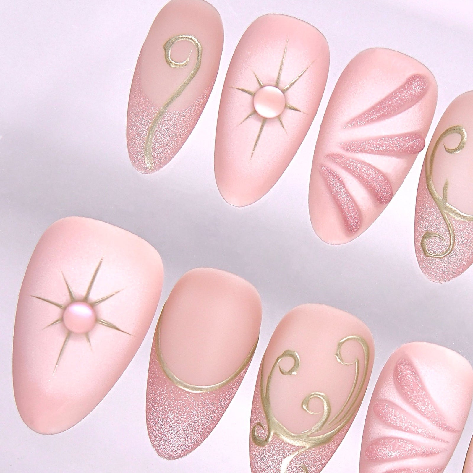 Close-up of Begin with Trust press-on nails showing gold celestial symbols and delicate blush pink base