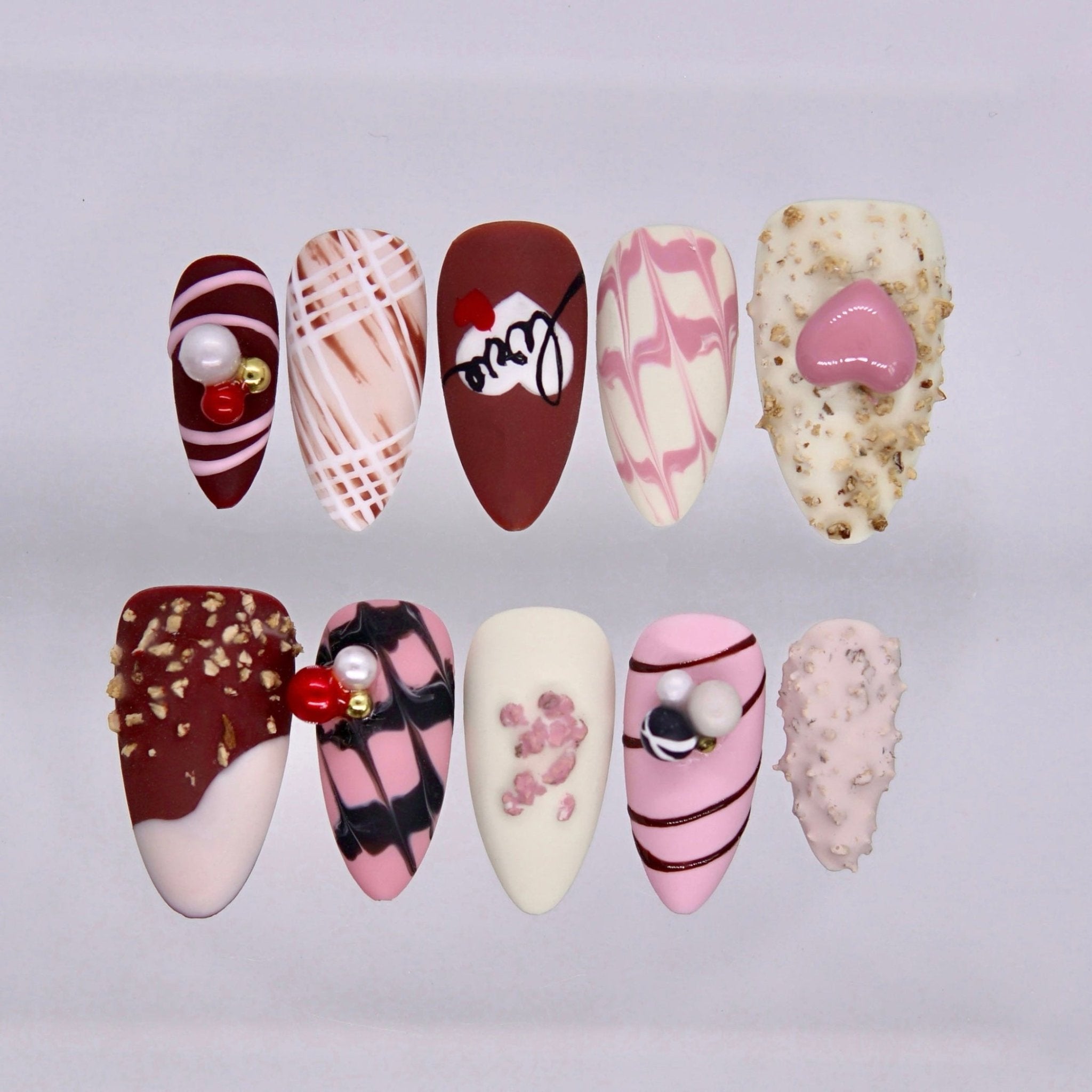 Handmade press on nails in berry red and cream tones with pearl accents and textured details displayed on a clear stand
