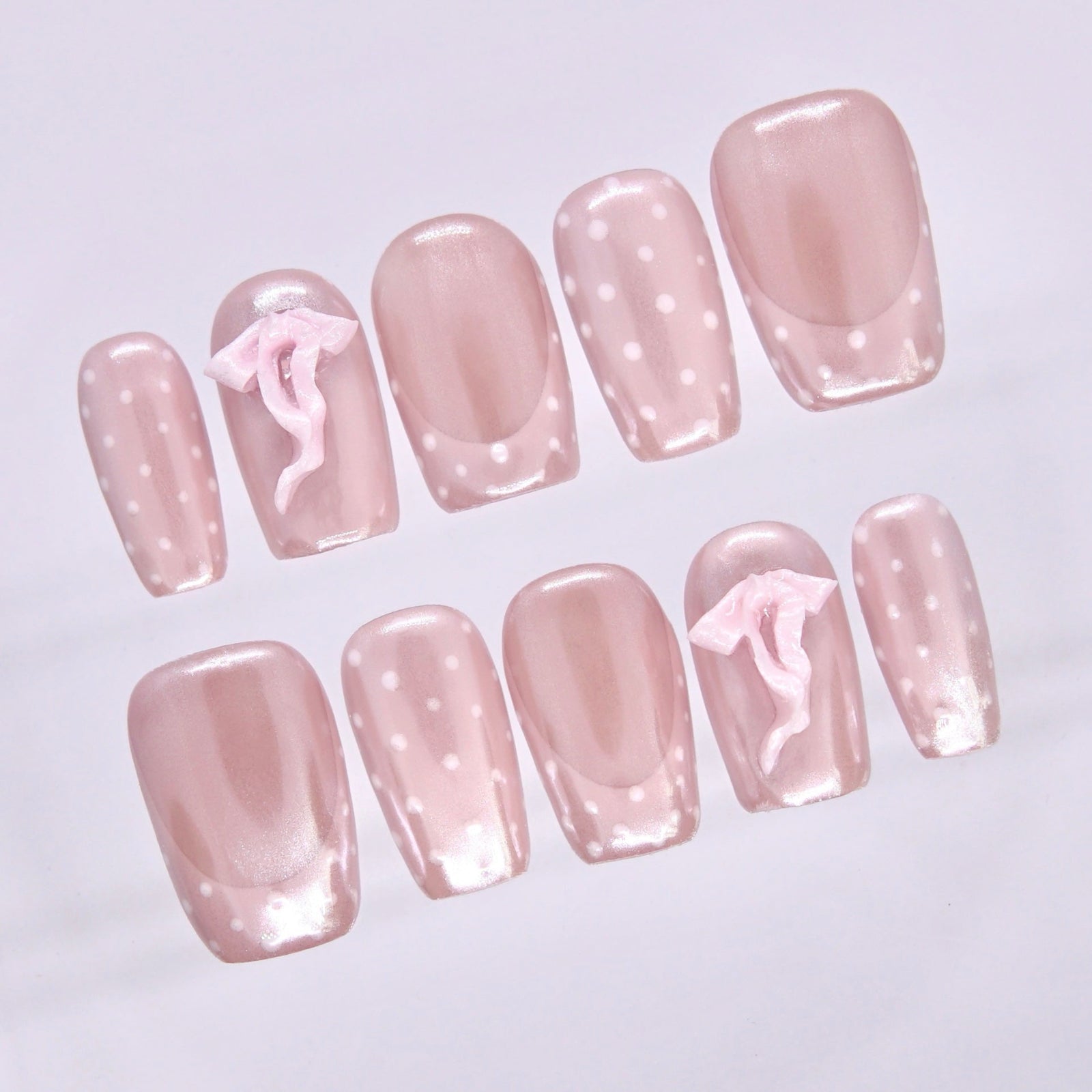 Close-up of Bliss Pig press-on nails featuring glossy blush shimmer, soft white polka dots, and pink 3D bow details.