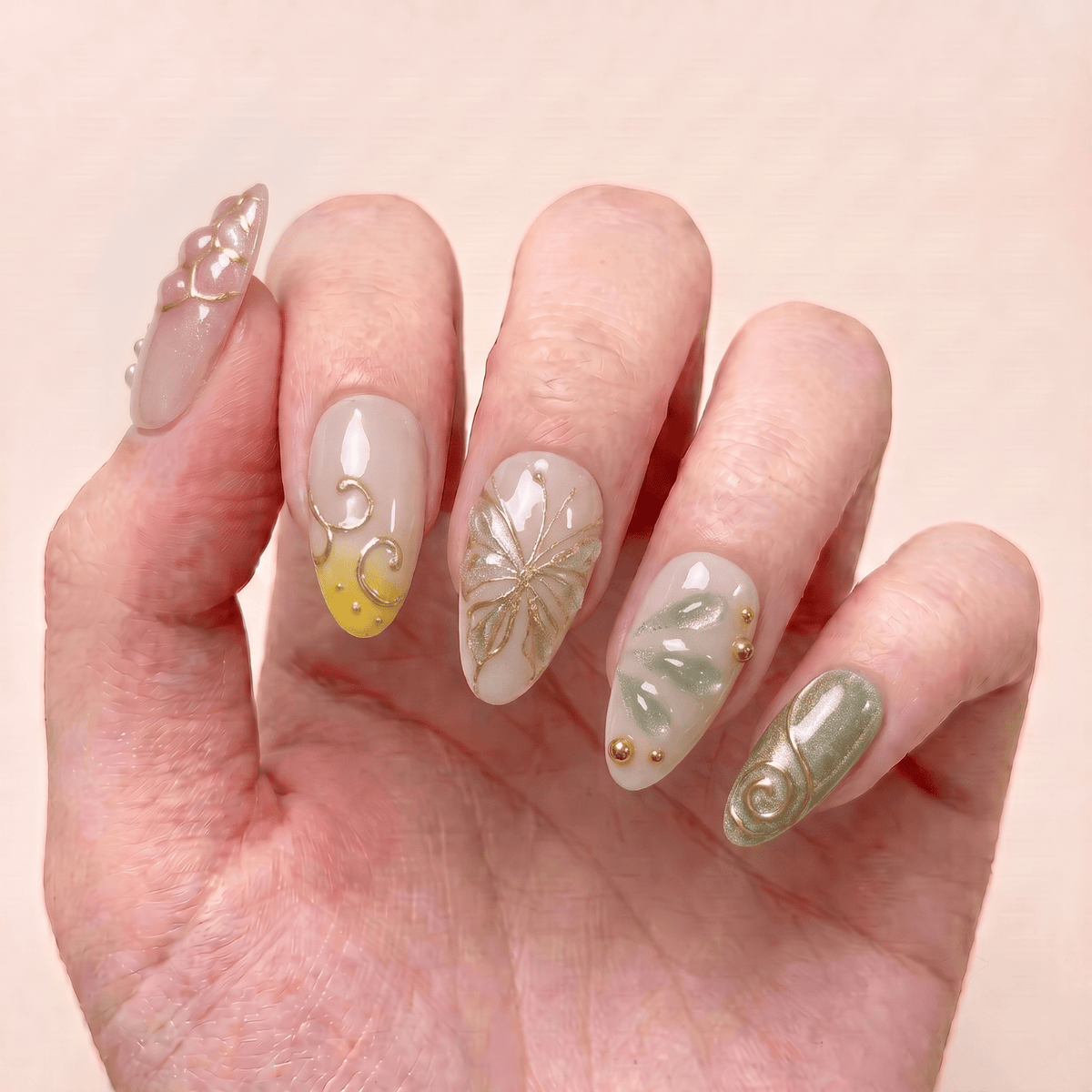 Butterfly Grove handmade press-on nails worn on hand with butterfly designs, pink, yellow and sage green tones, and delicate gold accents