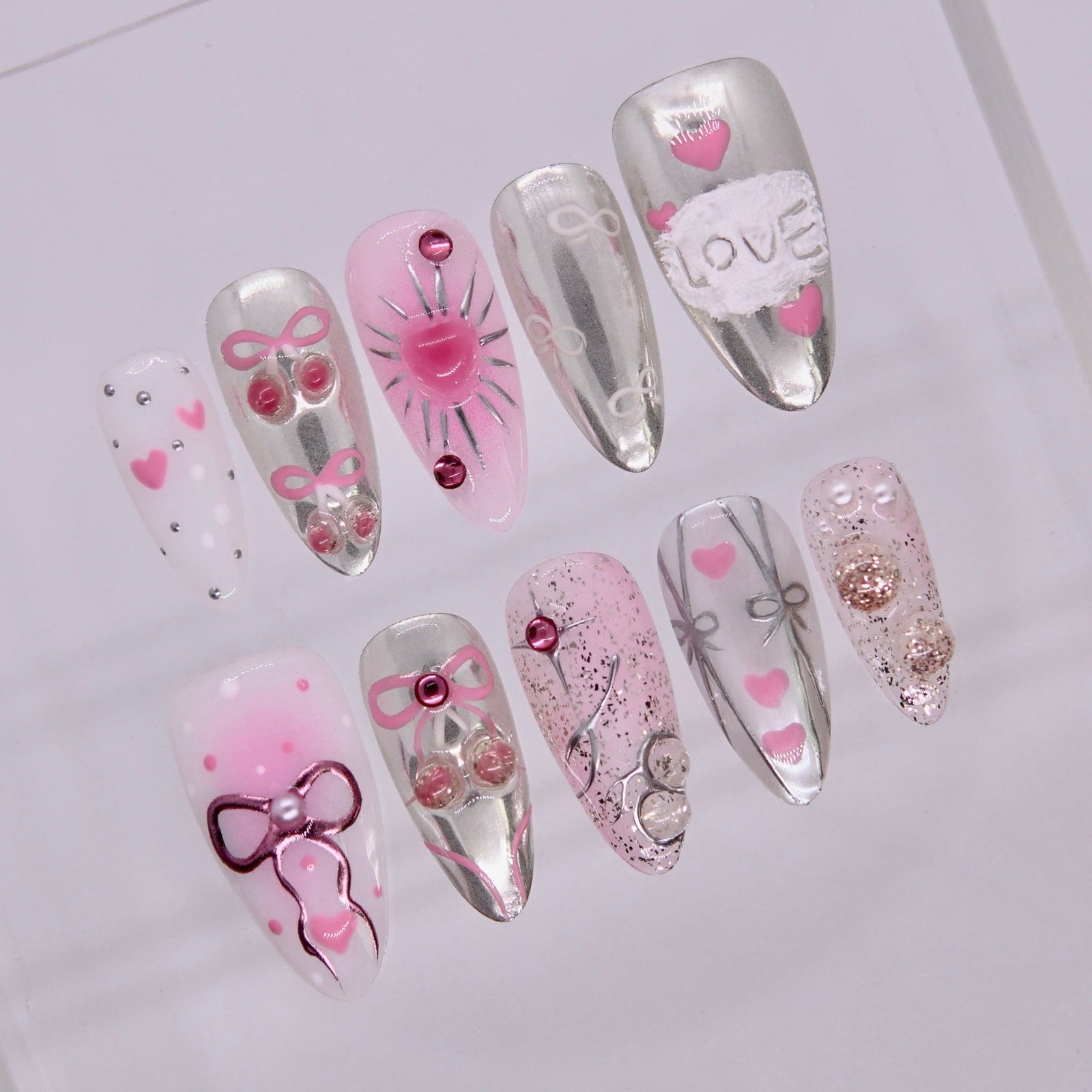 Close-up of Cherish Rat press-on nails showing silver chrome finish, pink heart designs, and glossy texture.
