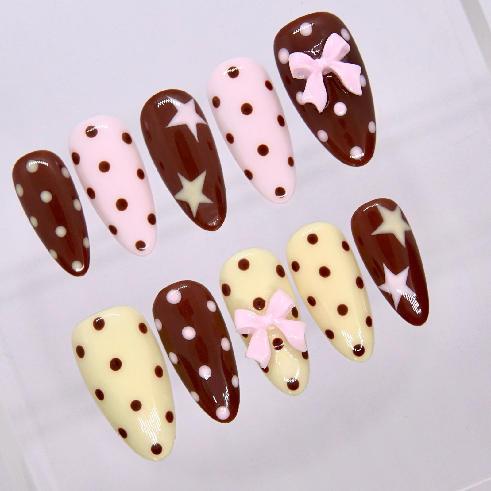 Close-up of Choco Daisy nails showing pastel pink bow and glossy chocolate dots.