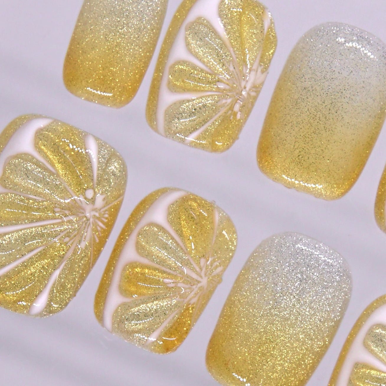 Detailed view of glossy lemon yellow press on nails with sparkling ombré finish and fruit slice nail art