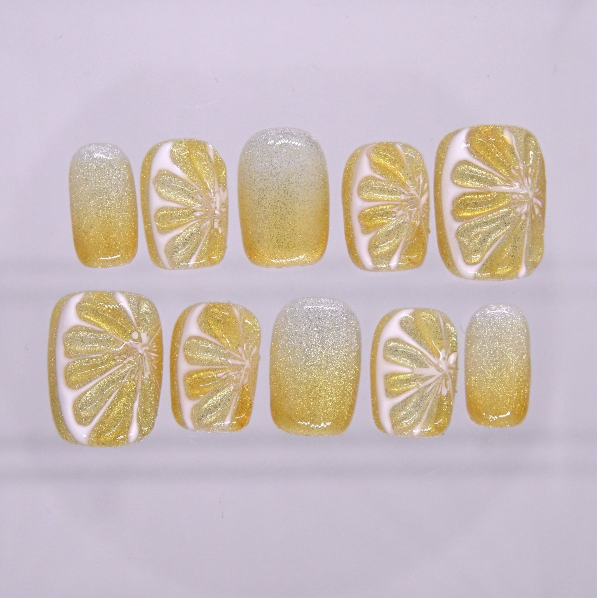 Short square press on nails with yellow glitter ombré and hand-painted citrus slice design on a soft glossy finish
