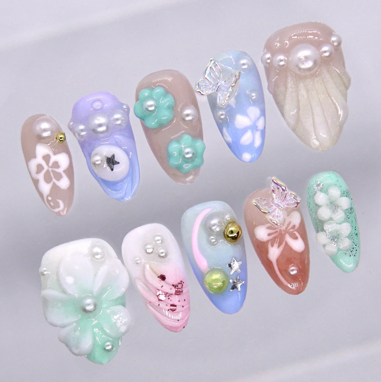 Close-up of pastel press on nails with glossy 3D floral details, pearl accents, butterfly embellishments, and whimsical charm-inspired design