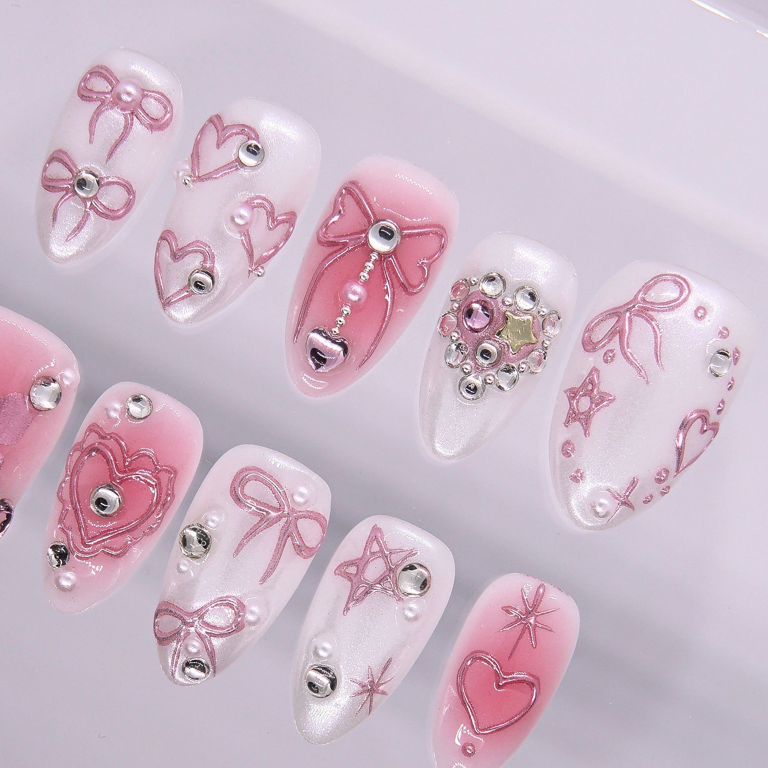 Close-up of sculpted bow and heart press-on nails with pearl and silver bead accents.