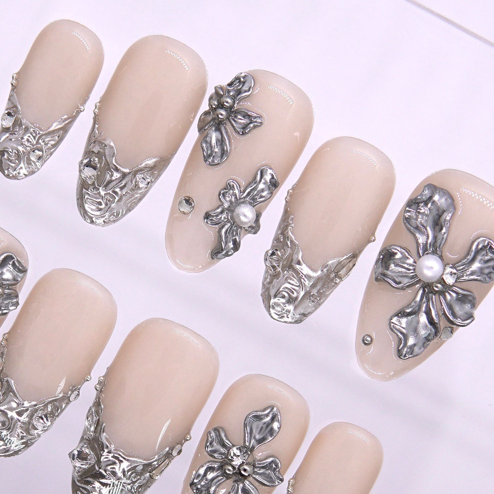 Macro view of silver cuticle detailing on a nude nail, highlighting architectural floral scrolls inspired by wedding lace and coastal stonework.