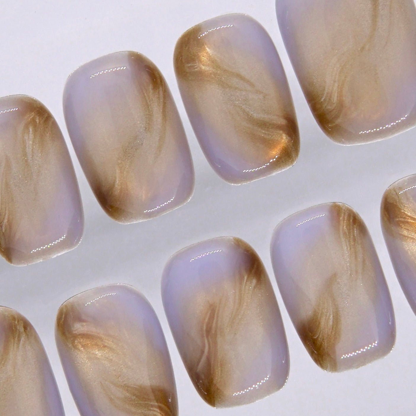 Detailed view of glossy short square press on nails with creamy beige tones and soft swirling brown accents