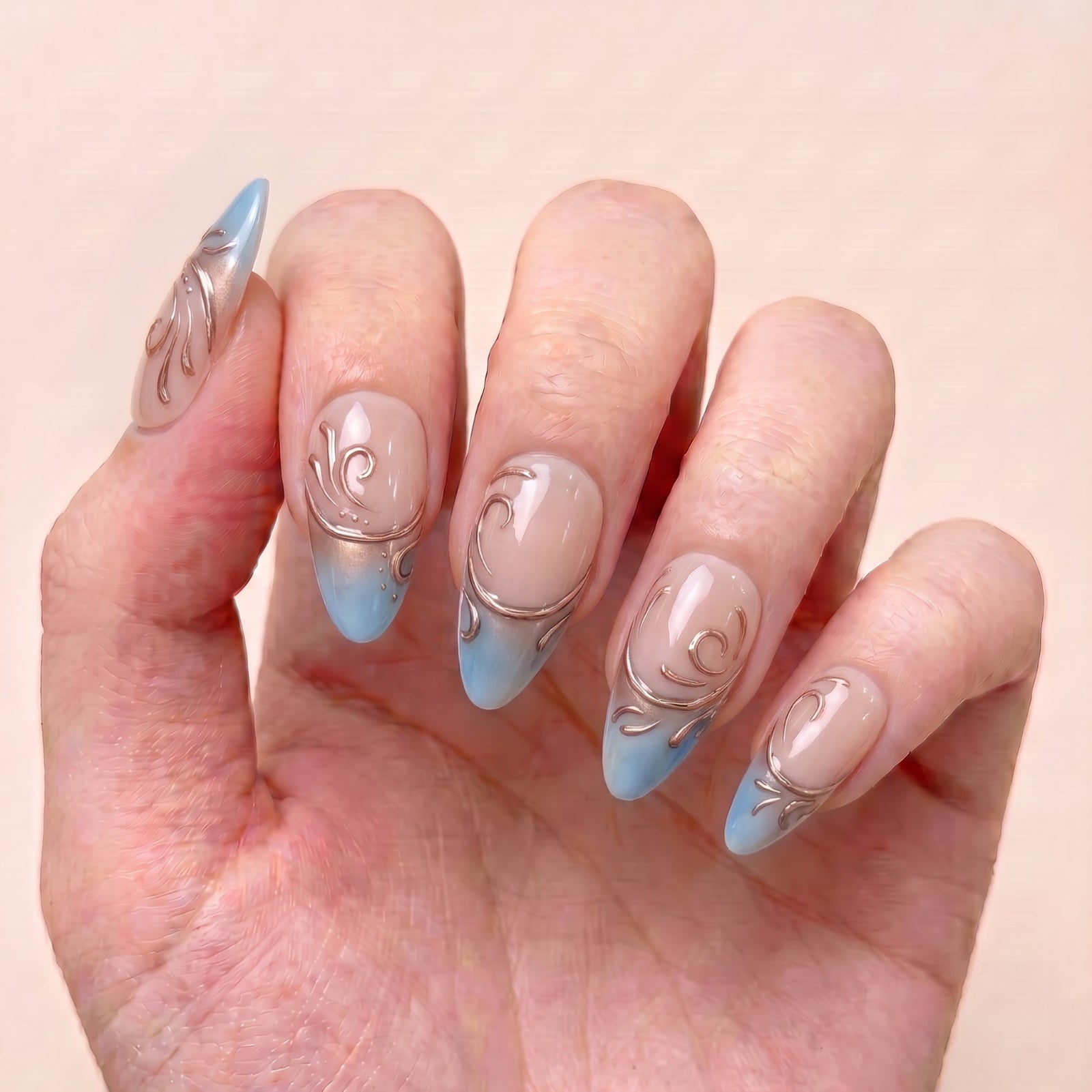 Duskwater Script handmade press-on nails worn on hand with nude bases, blue French tips, and elegant copper-gold swirl nail art