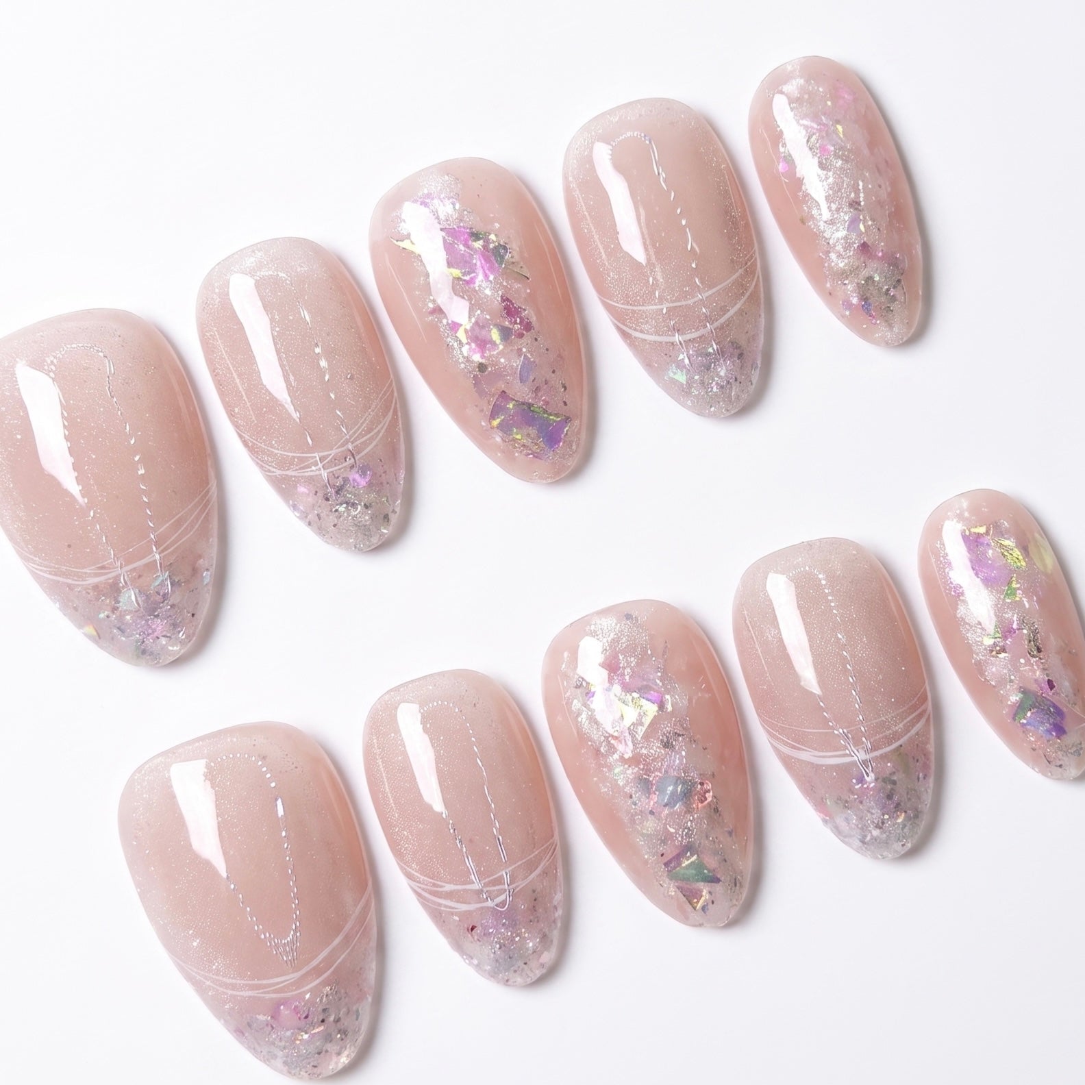 Close-up of Fairydust Whisper press-on nails featuring translucent blush pink bases and reflective pink iridescent foil flakes