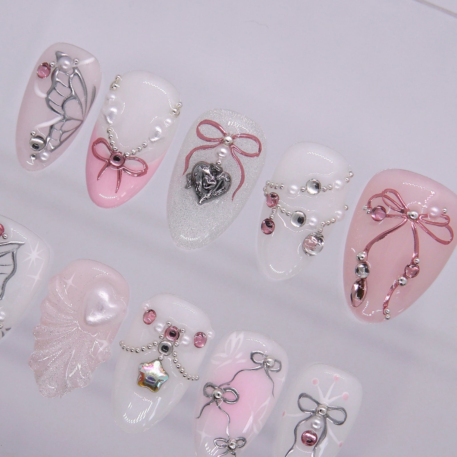 Pink and white press on nails with bow and heart details for a girly look.