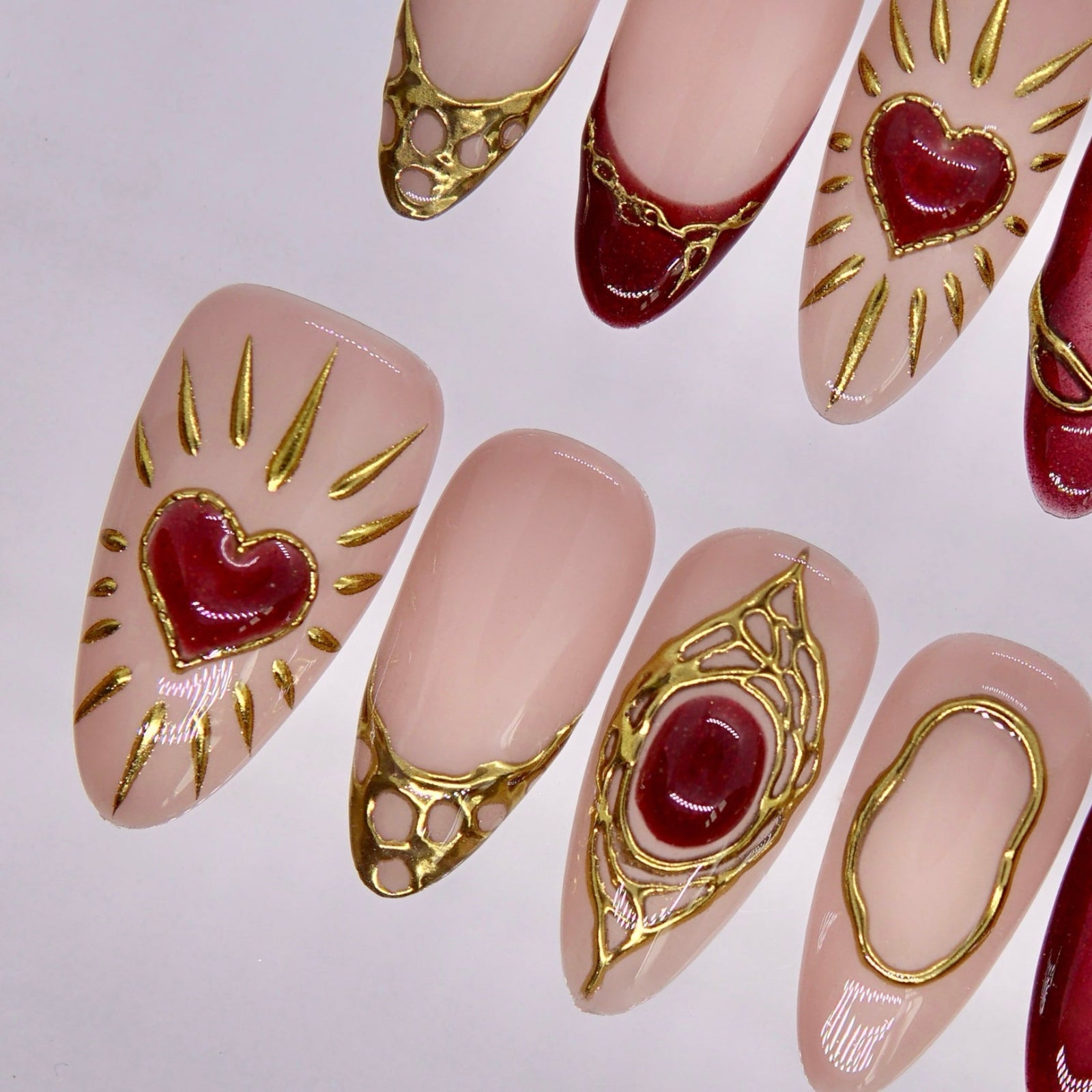 Detail view of Dragon zodiac nails showing deep crimson tips, gold edging, and a gold rose accent on glossy nude nails.