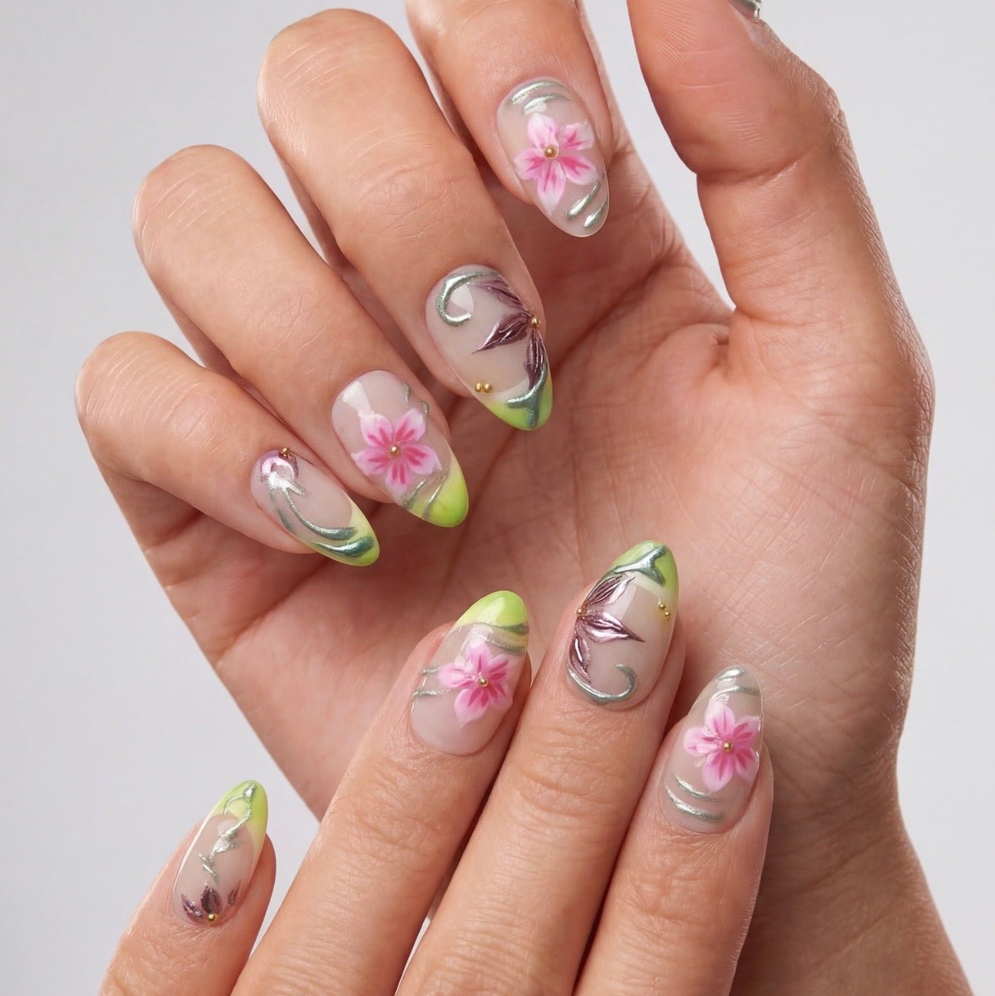 Model wearing almond floral press on nails with lime green French tips and pink flower details in a soft spring-inspired lifestyle setting